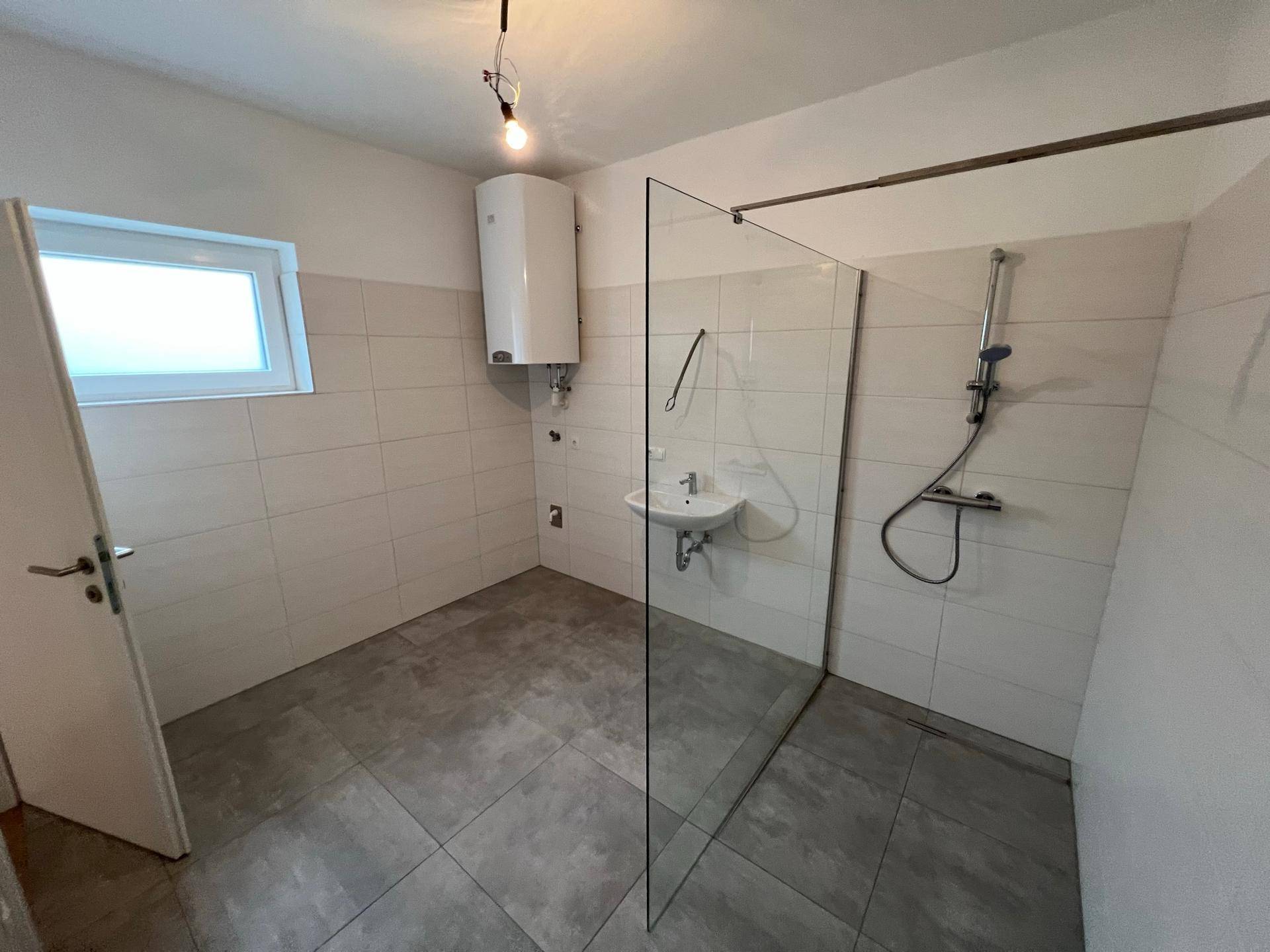 Modernes Badezimmer mit großer, ebenerdiger Dusche, Waschbecken und hellen Wandfliesen.