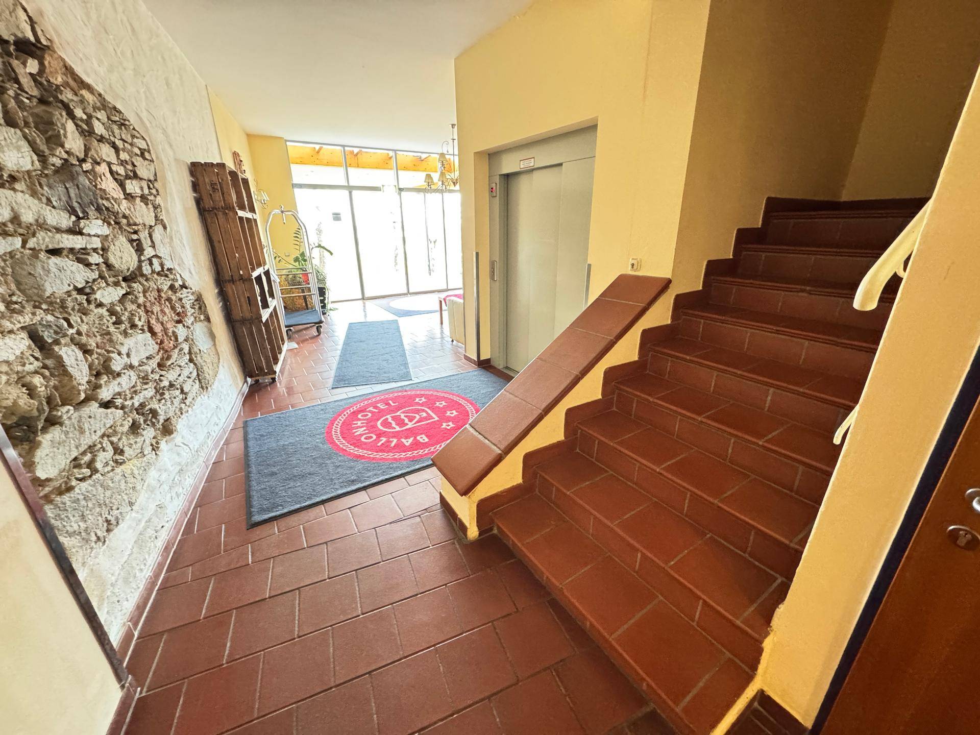 Eingangsbereich mit Treppe, Aufzug und gefliestem Terrakottaboden.