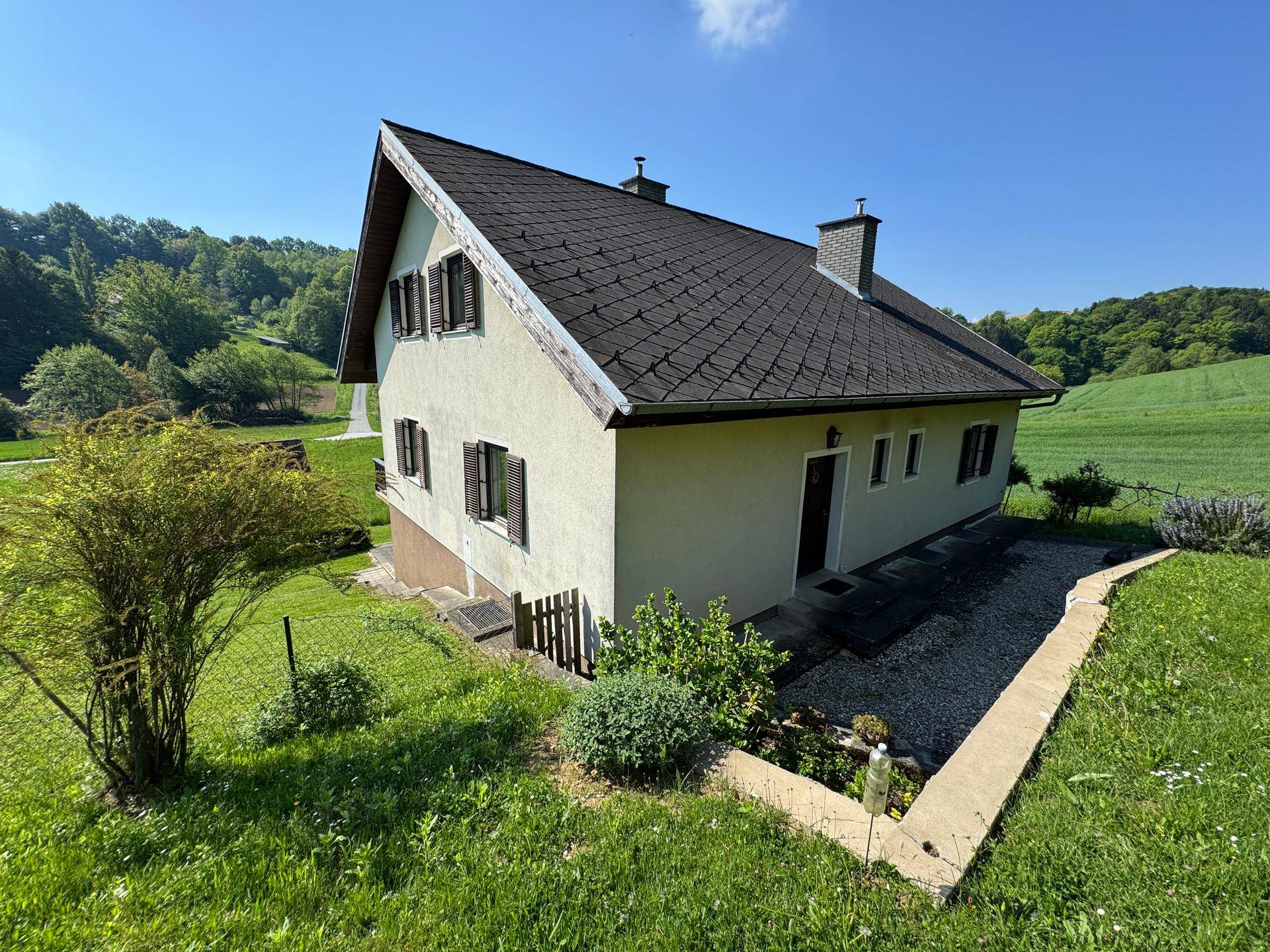 Erhöhte Seitenansicht des Hauses mit Garten und umliegender grüner Landschaft.