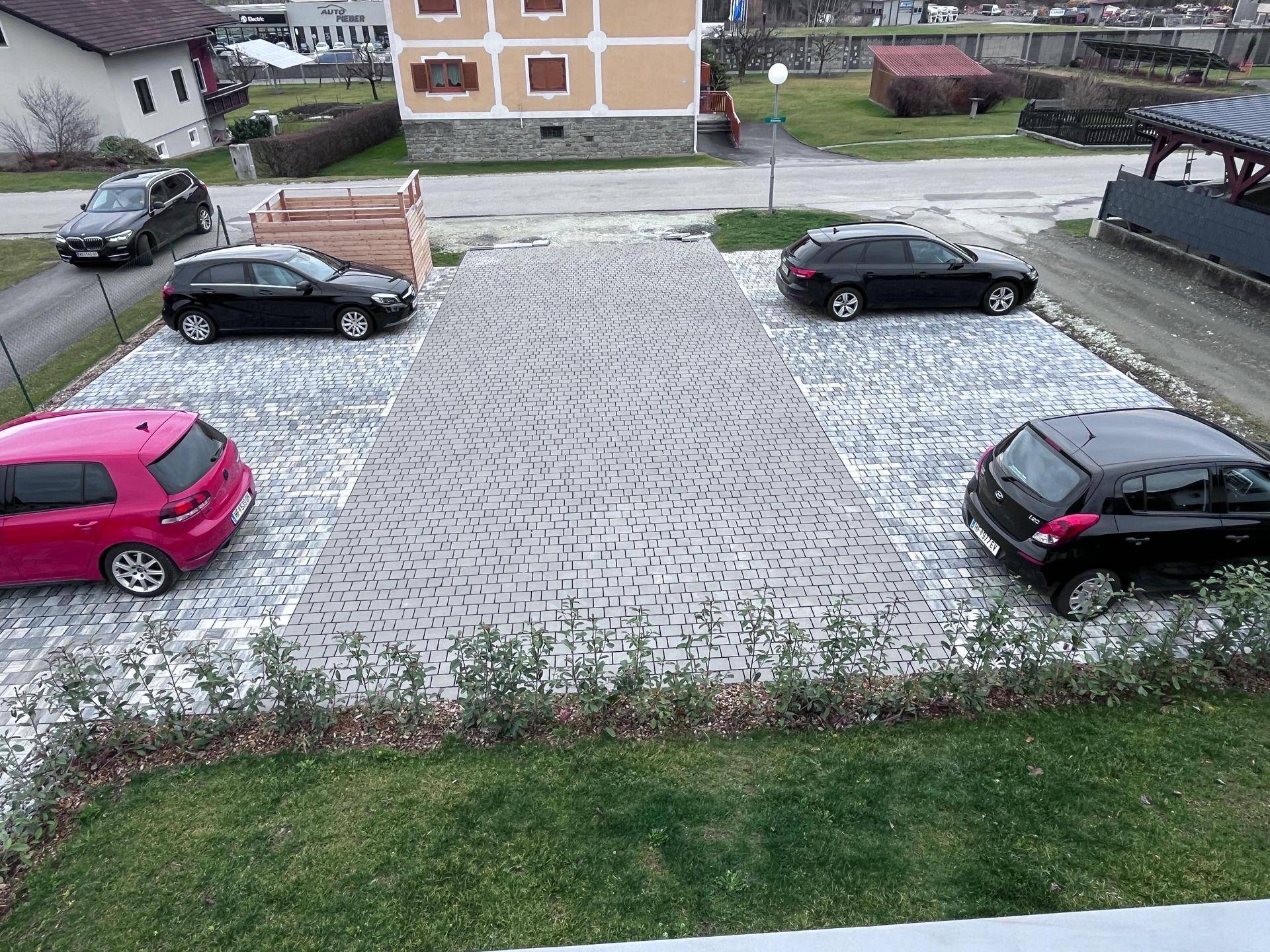 Außenansicht des Parkplatzes mit gepflasterten Stellflächen und mehreren geparkten Autos.