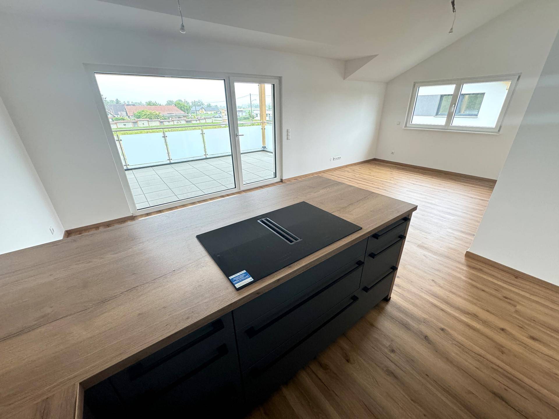 Offene Küche mit Kochinsel, Induktionskochfeld und Zugang zu einem großen Balkon.