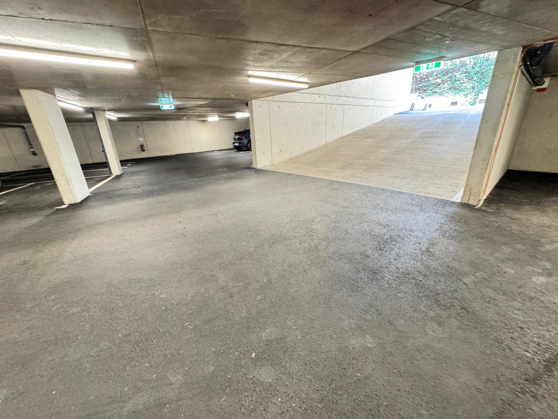 Geräumige Tiefgarage mit Betonwänden und hellen Leuchtstoffröhren, bietet sichere Parkmöglichkeiten.