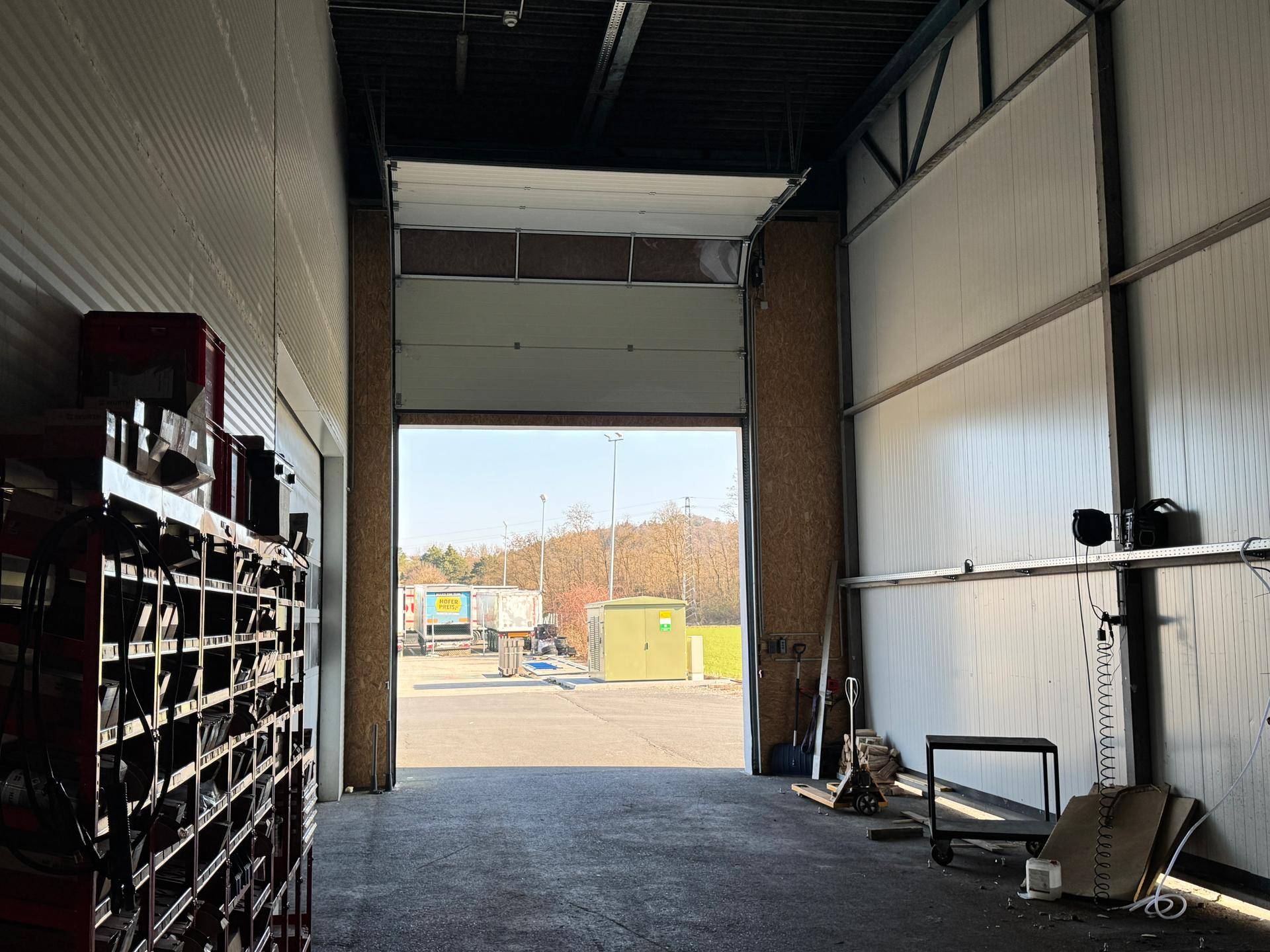 Blick aus der Halle durch ein geöffnetes Rolltor auf den Außenbereich und die Zufahrt.