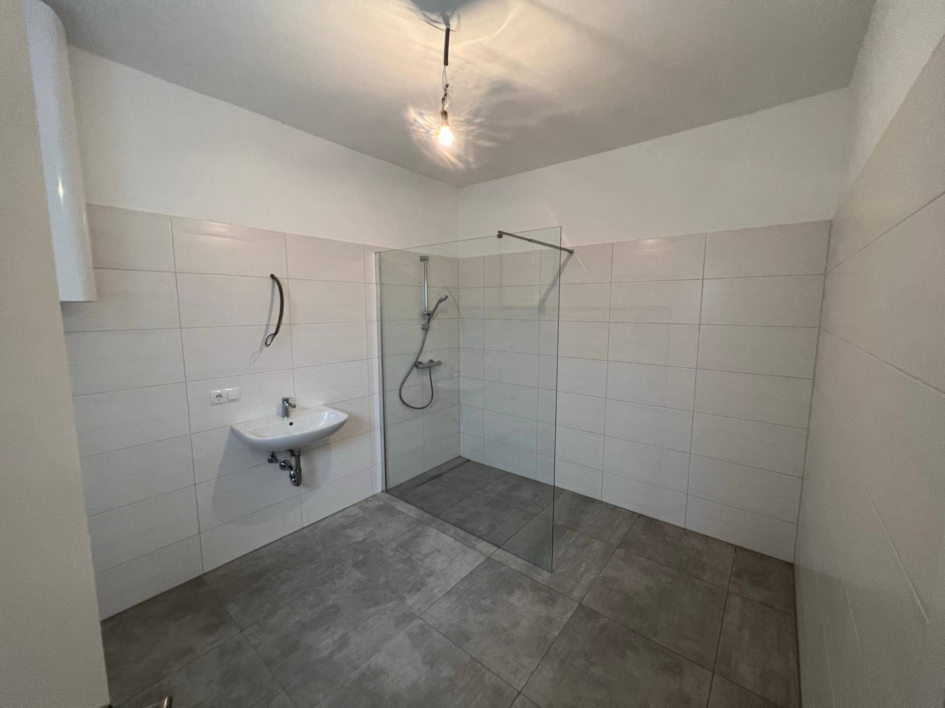 Modernes Badezimmer mit großer, ebenerdiger Dusche, Waschbecken und hellen Wandfliesen.