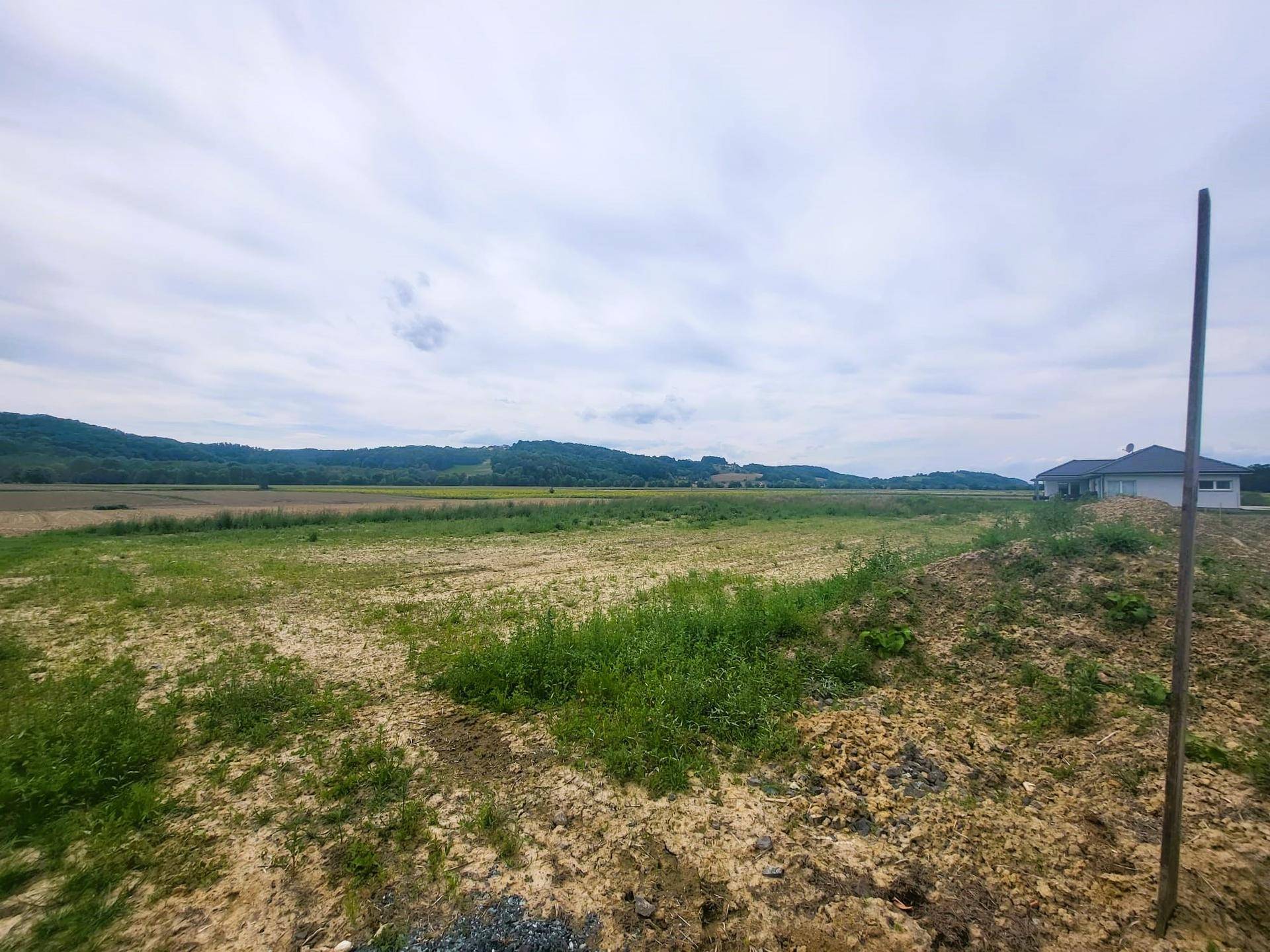 Weitläufige Landschaft mit Feldern, grünen Hügeln und einem Haus am Horizont.