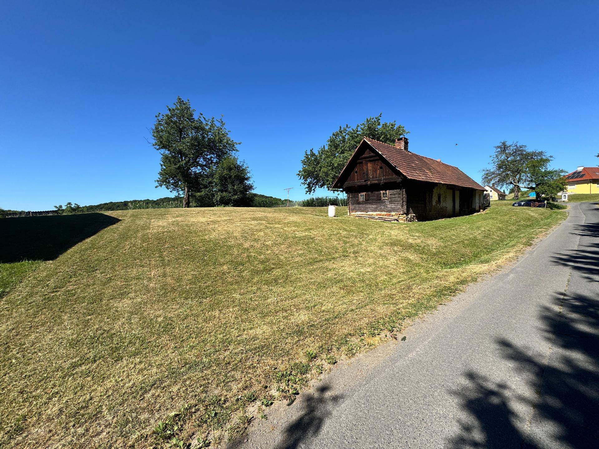 Rustikales Holzhaus mit Ziegeldach an einer Straße, umgeben von grünen Hügeln.