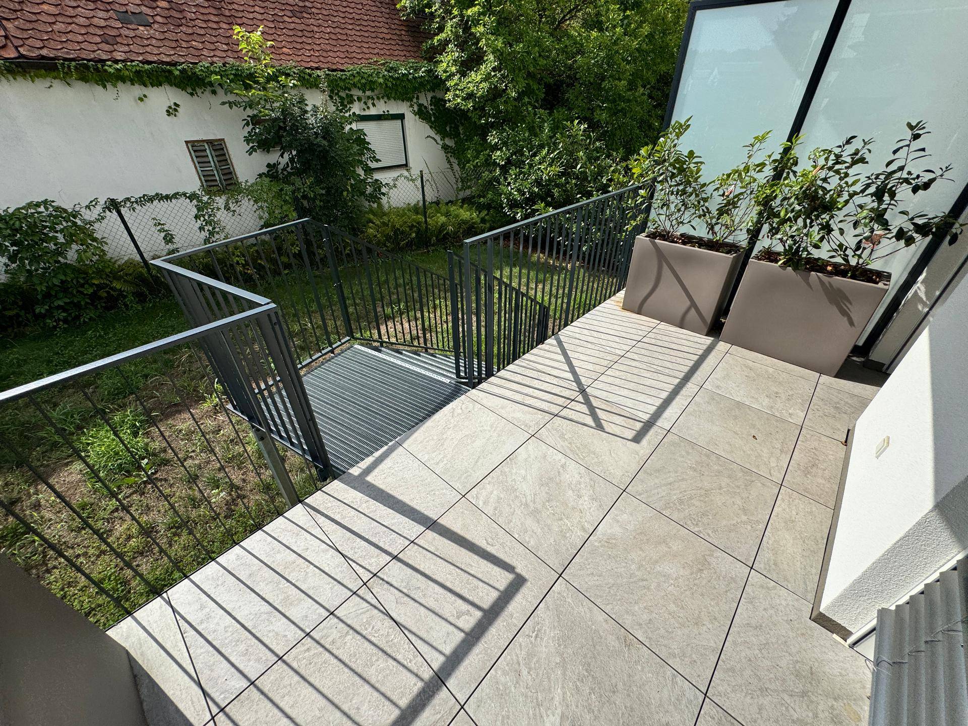 Terrasse mit Metallgeländer und Treppe, die zum Gartenbereich führt, ideal für den Außenbereich.