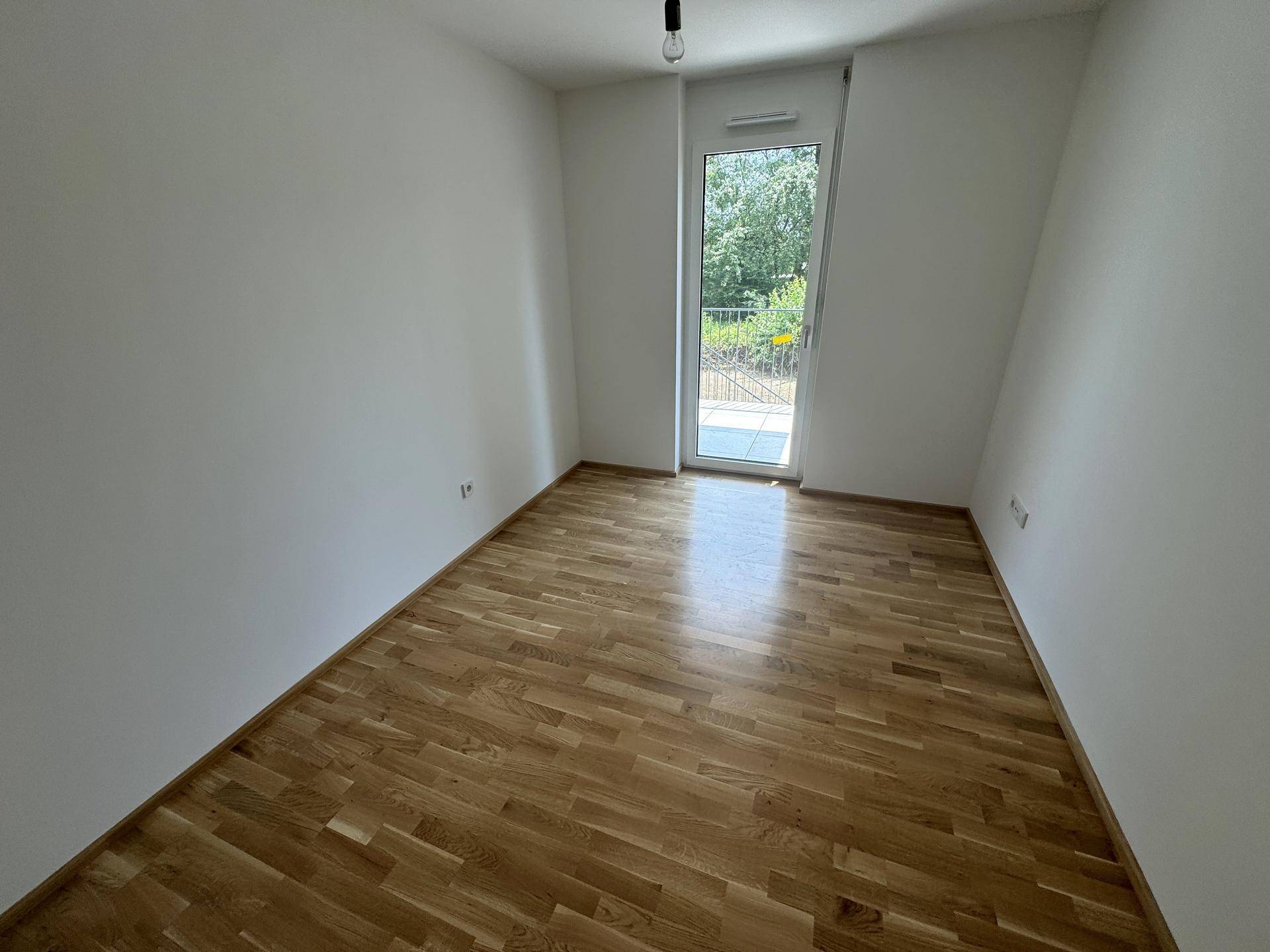 Helles Zimmer mit Holzboden und Zugang zu einem kleinen Außenbereich.