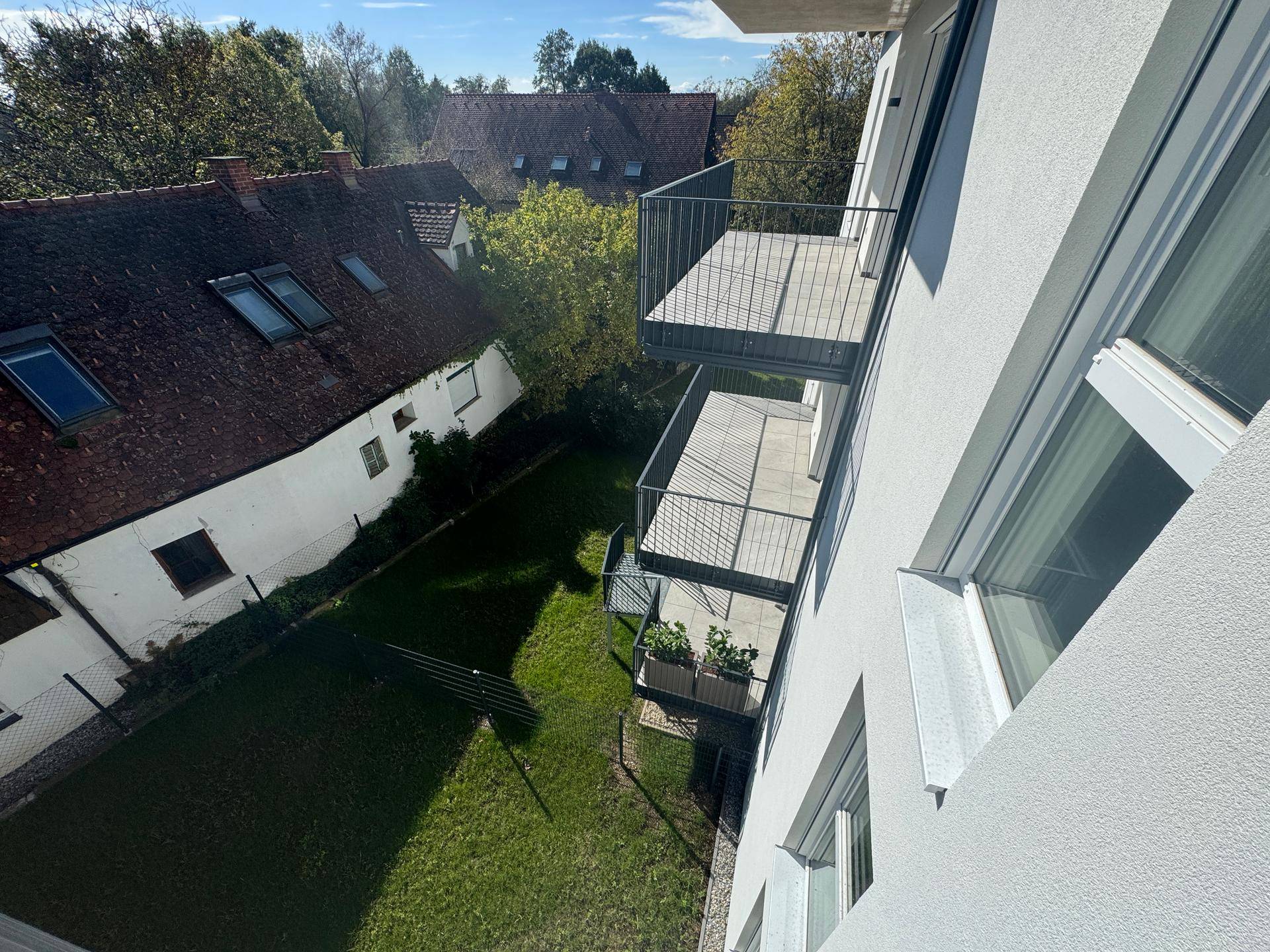 Balkone eines Neubaus mit Blick auf einen grünen Garten und traditionelle Nachbargebäude.