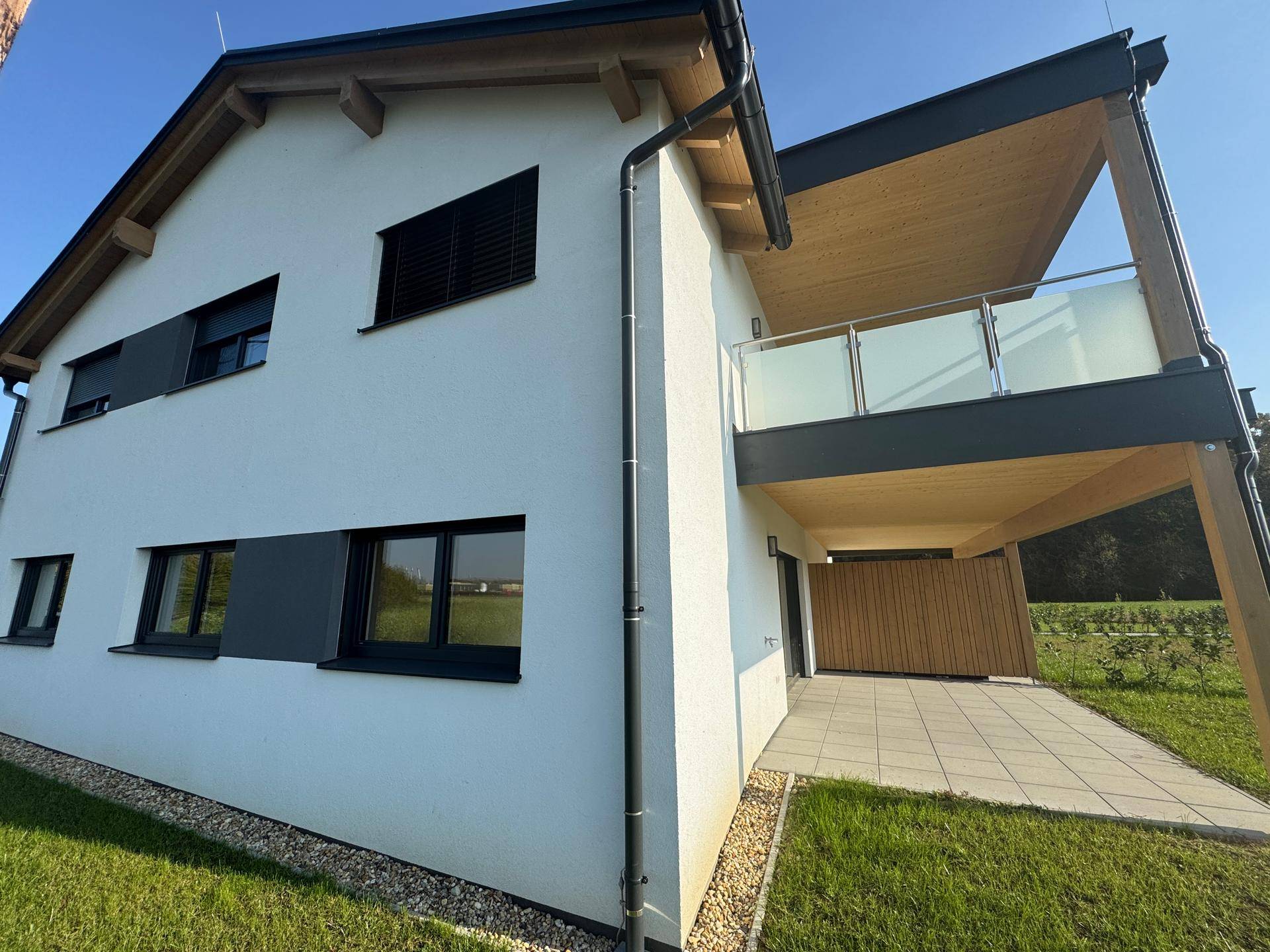 Moderne Doppelhaushälfte mit Terrasse und Balkon, umgeben von viel Grün.