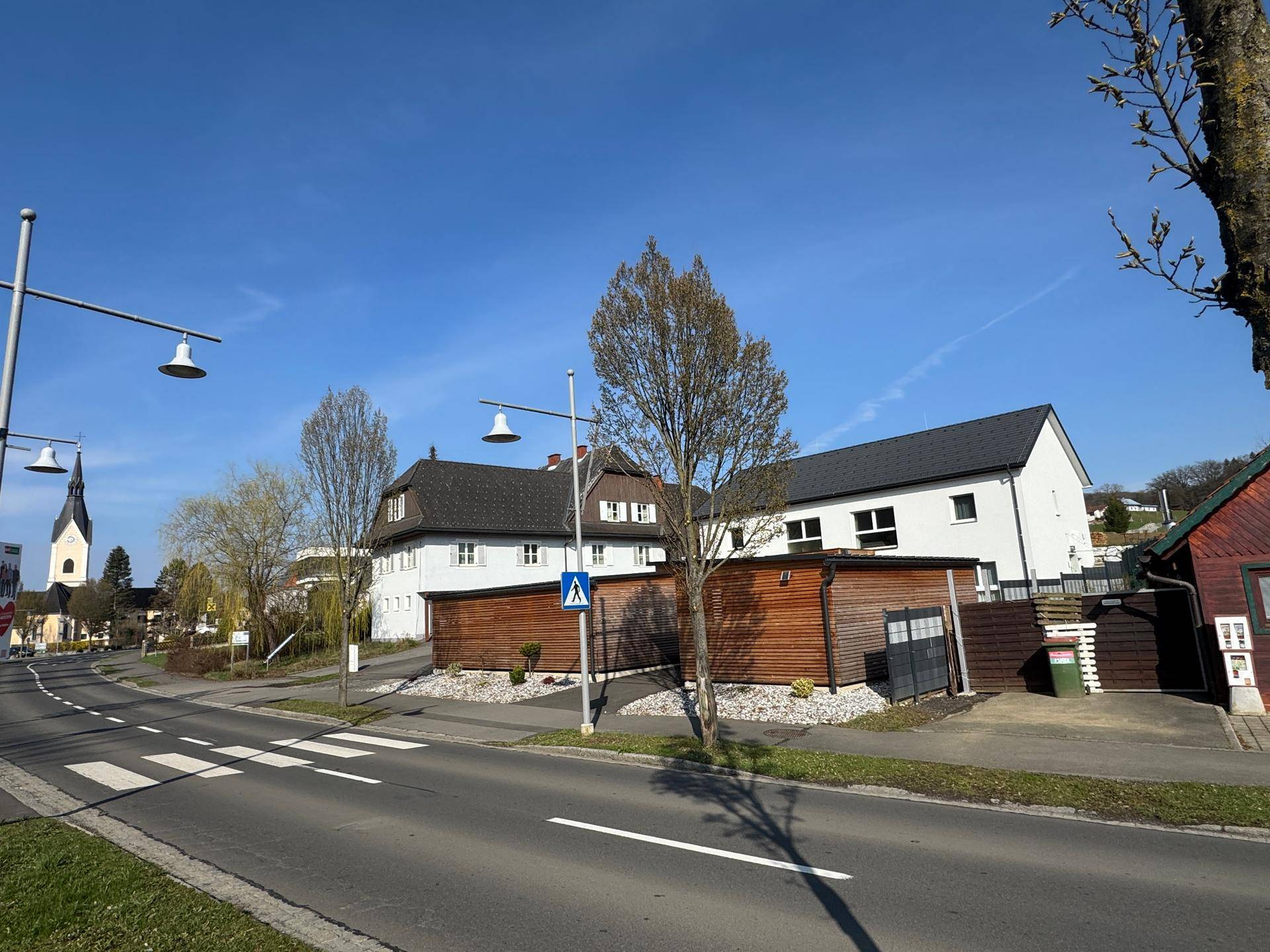Blick auf die Straße mit angrenzenden Gebäuden und einem Kirchturm in der Ferne.