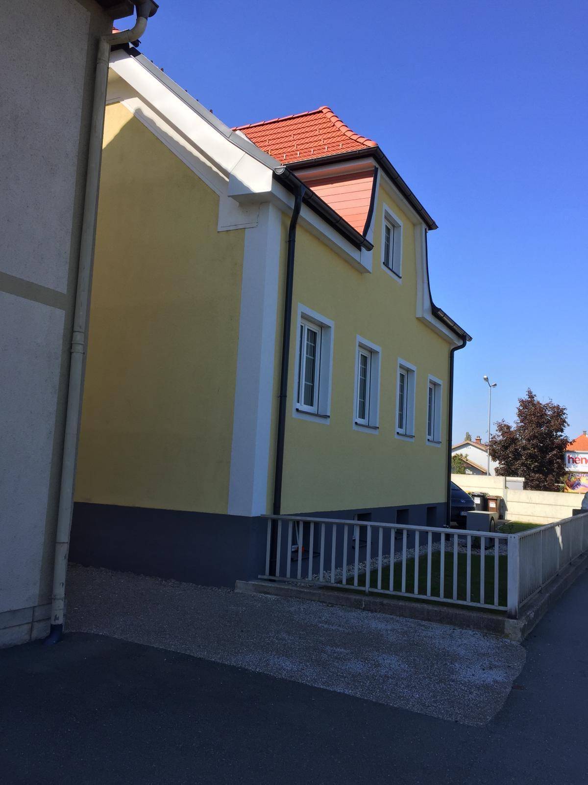 Seitenansicht des frisch renovierten Hauses mit gelber Fassade und rotem Ziegeldach.