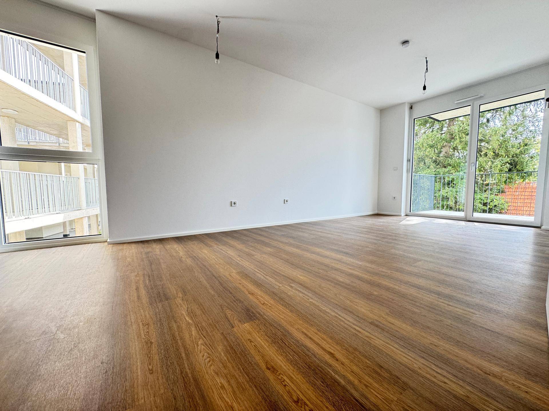 Geräumiges, helles Wohnzimmer mit Laminatboden, großen Fenstern und Zugang zu einem Balkon.