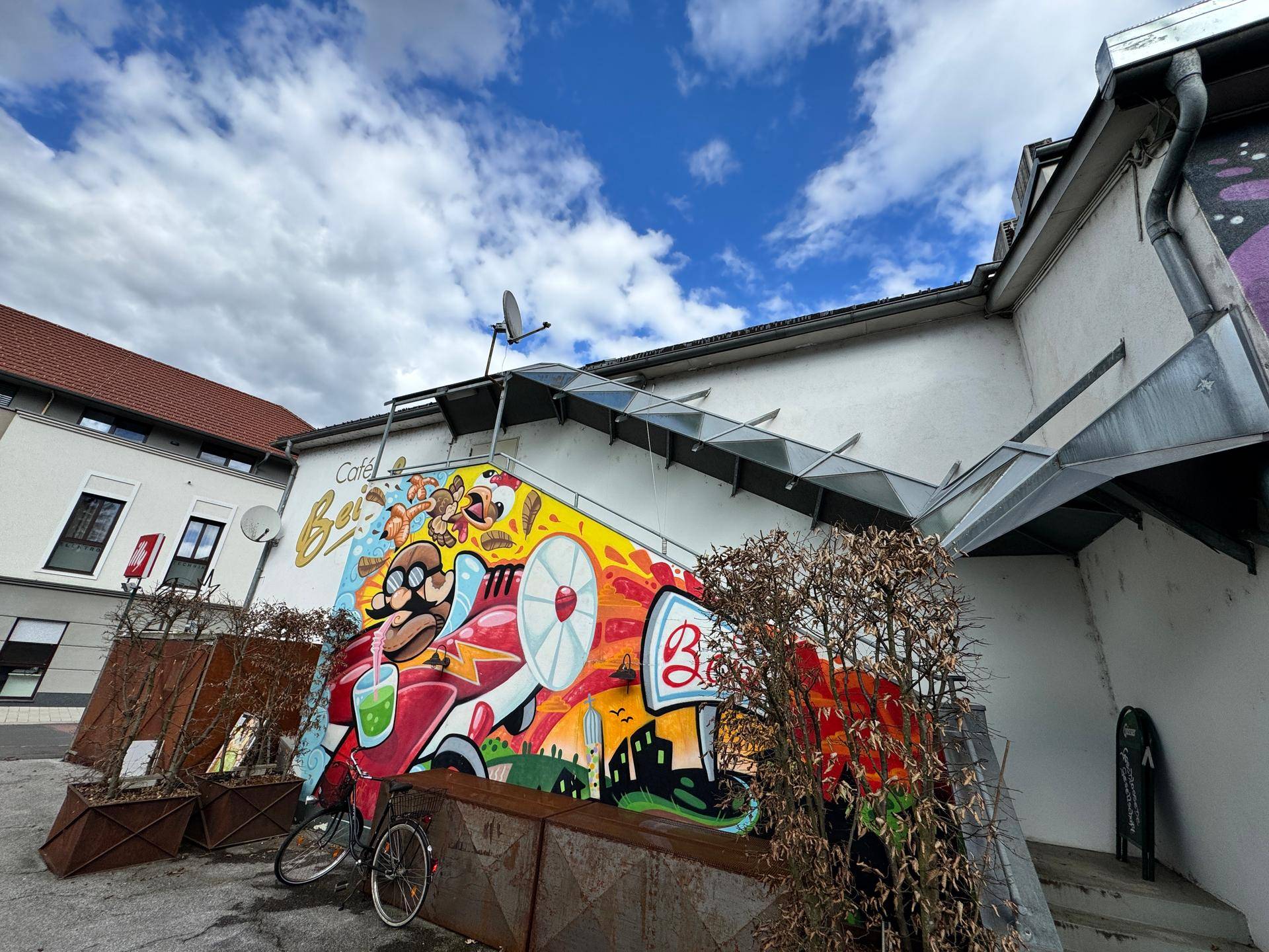 Fassade mit großflächigem Graffiti und einem überdachten Treppenaufgang, der zum Gebäude führt.