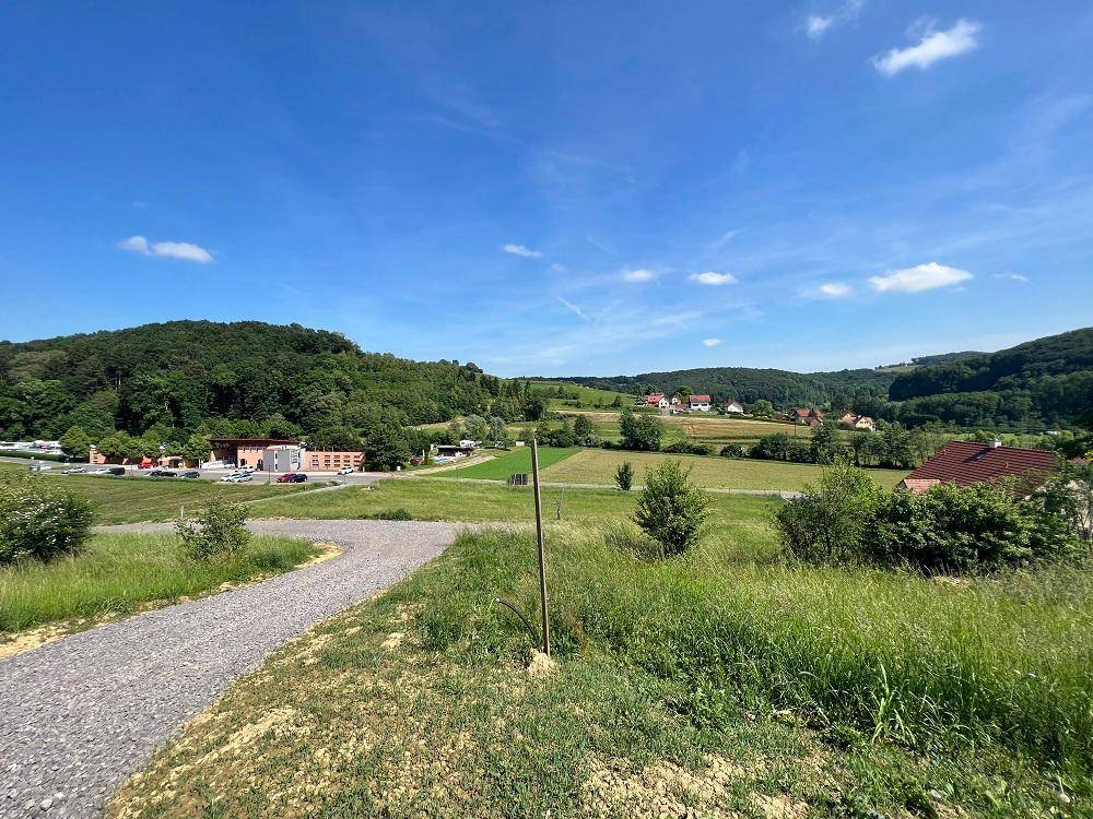 Sonniger Ausblick auf eine ländliche Gegend mit Feldern, Wäldern und einem kleinen Dorf.