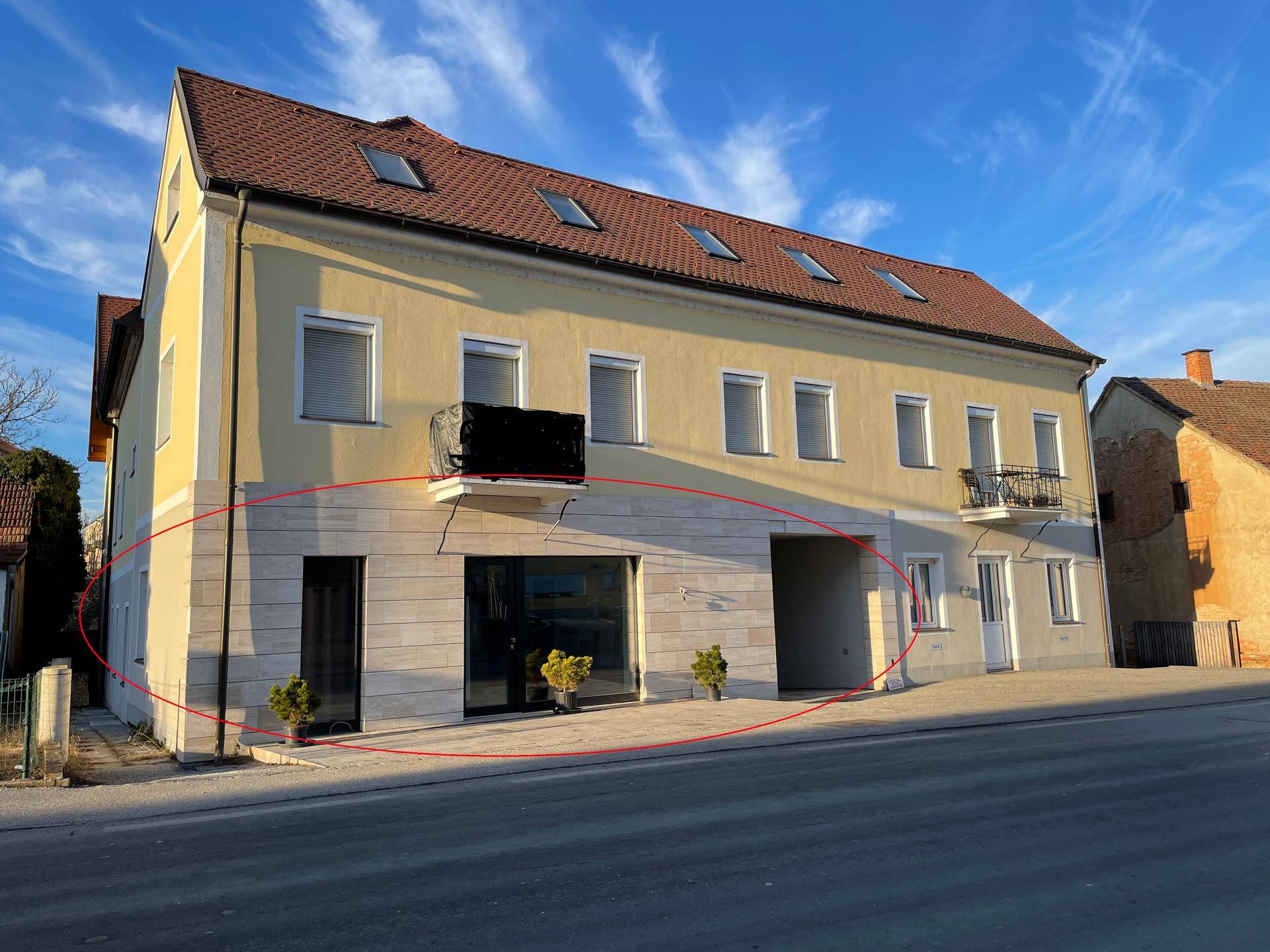 Gelbes Gebäude mit rotem Dach und modernisierter Erdgeschossfassade, die einen Geschäftsraum hervorhebt.