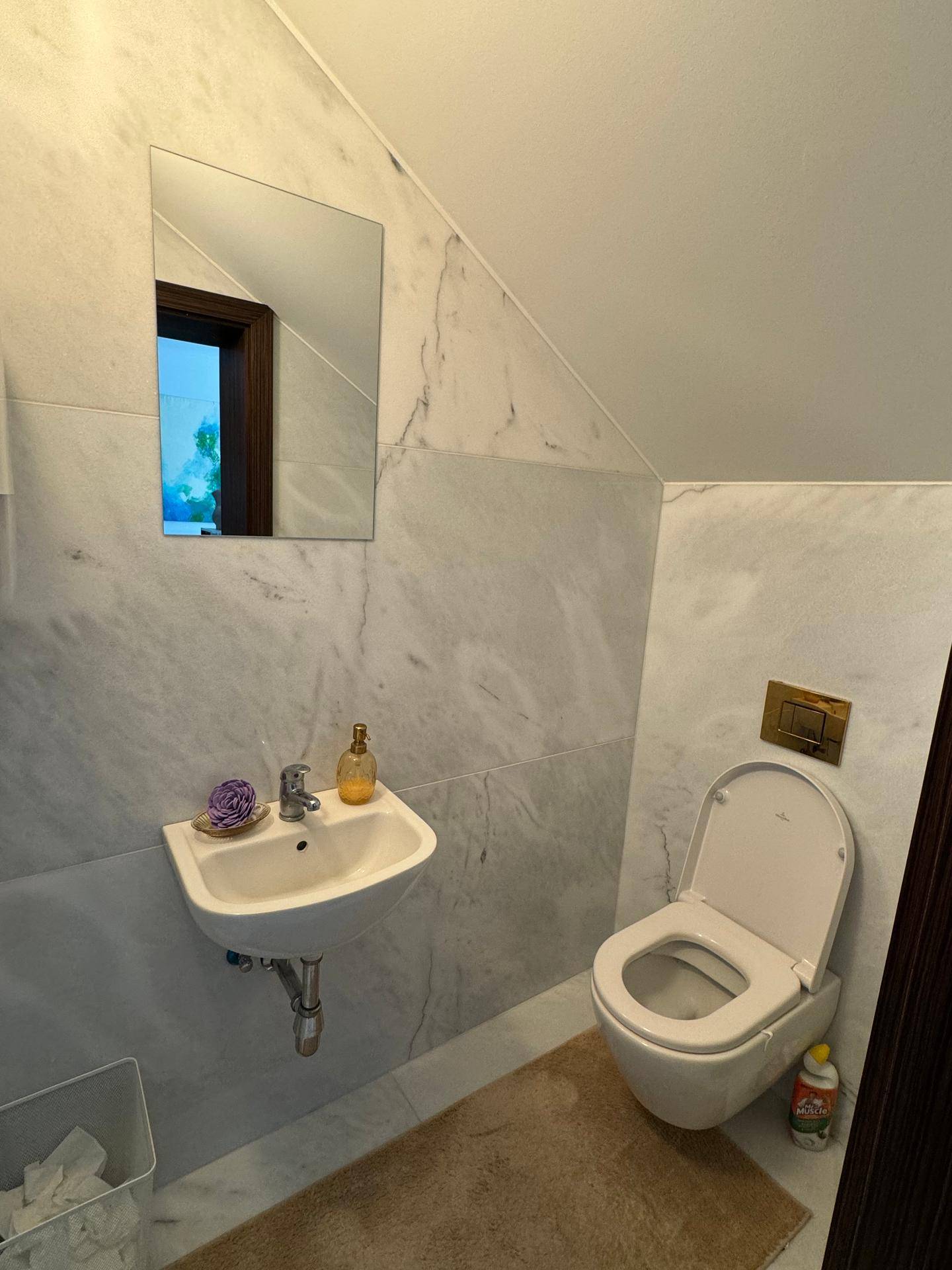 Kleines WC mit Marmorfliesen, wandmontierter Toilette und Waschbecken unter einer Dachschräge.