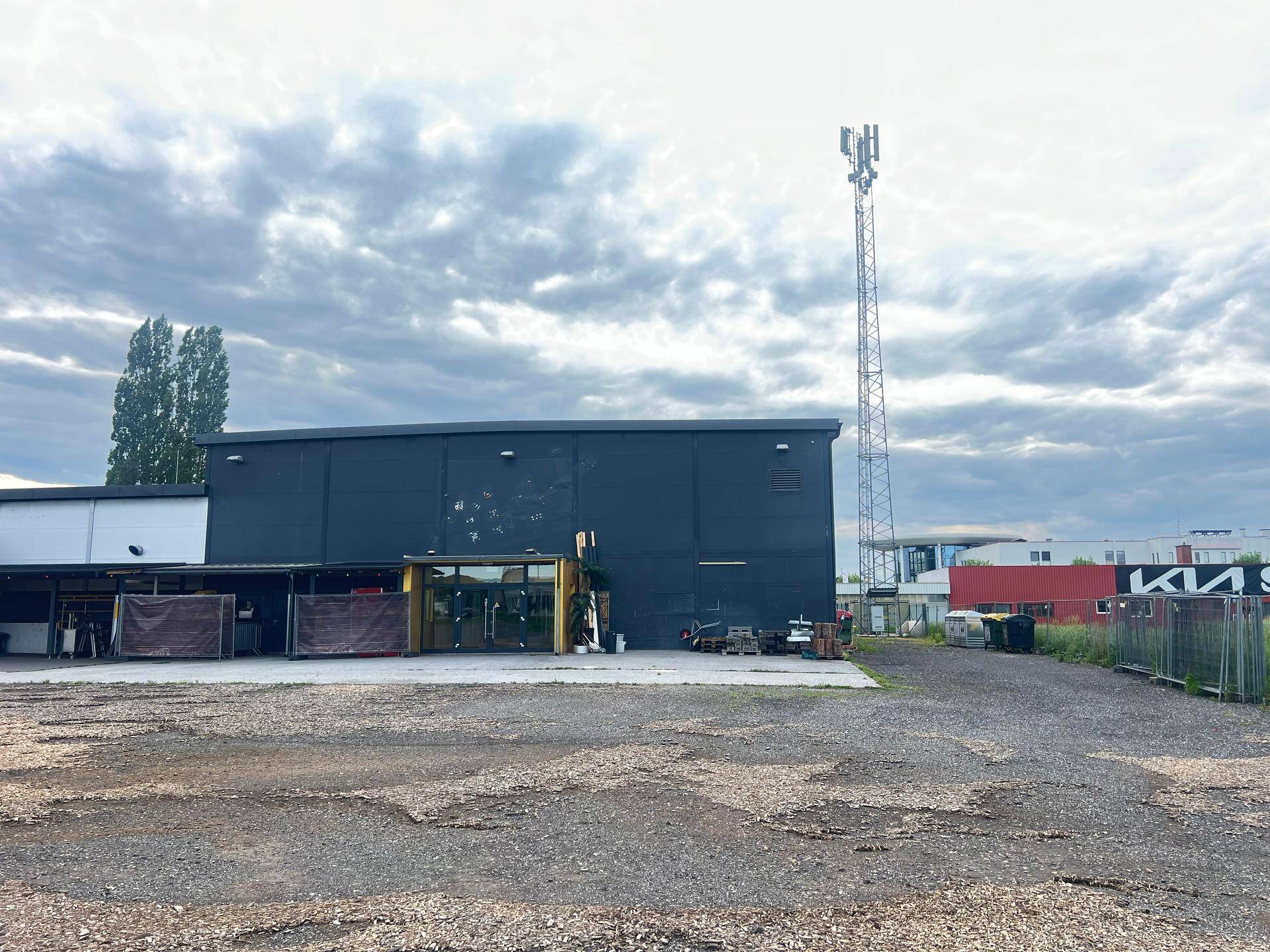 Rückansicht des Geschäftsgebäudes mit großem Schotterparkplatz und Mobilfunkmast.