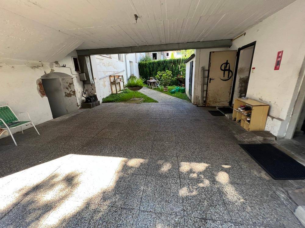 Überdachter Außenbereich mit Zugang zu einem begrünten Innenhof und weiteren Gebäudeteilen.