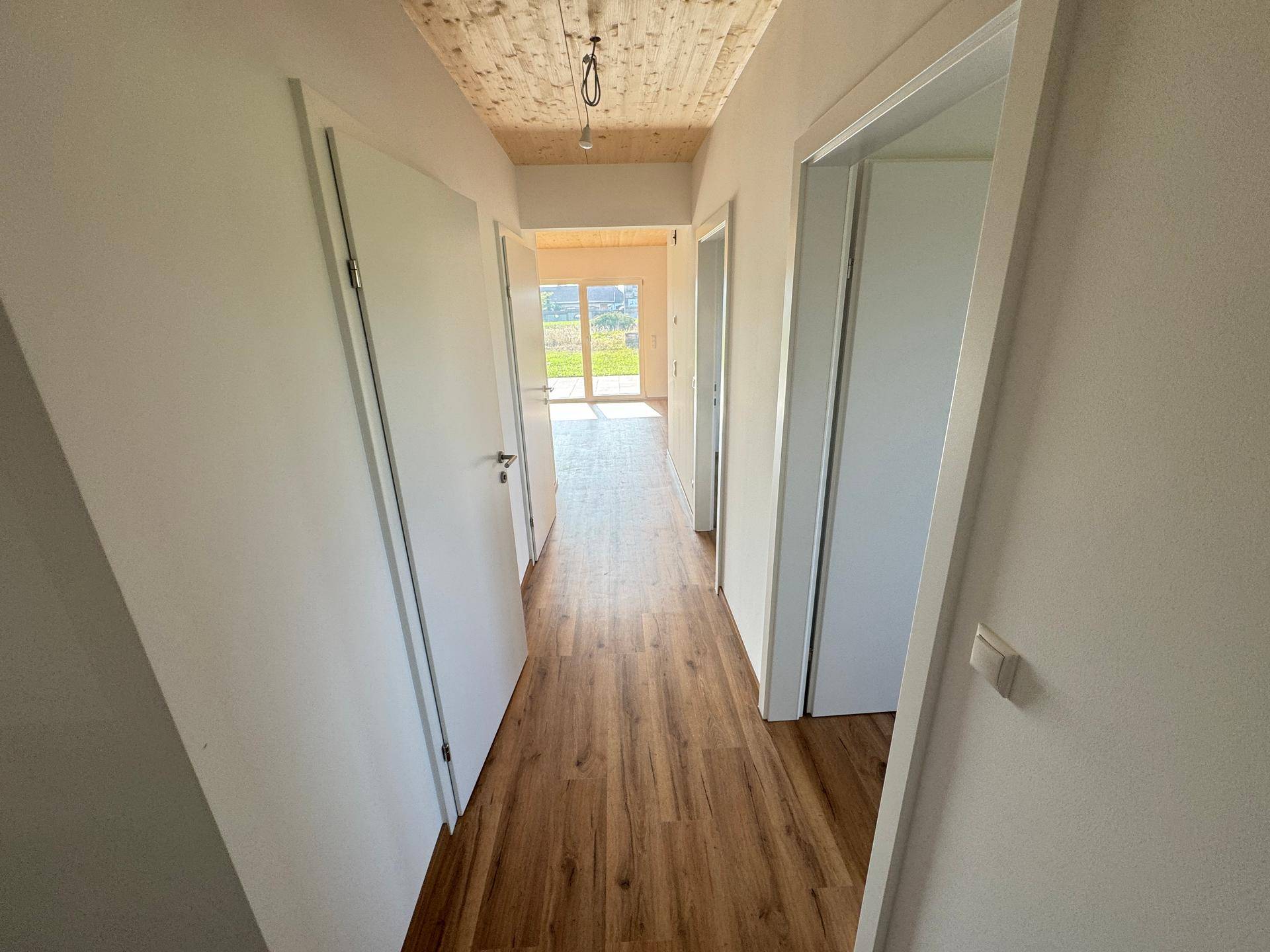Heller Flur mit Holzbalkendecke und Laminatboden, der zu den Wohnbereichen führt.