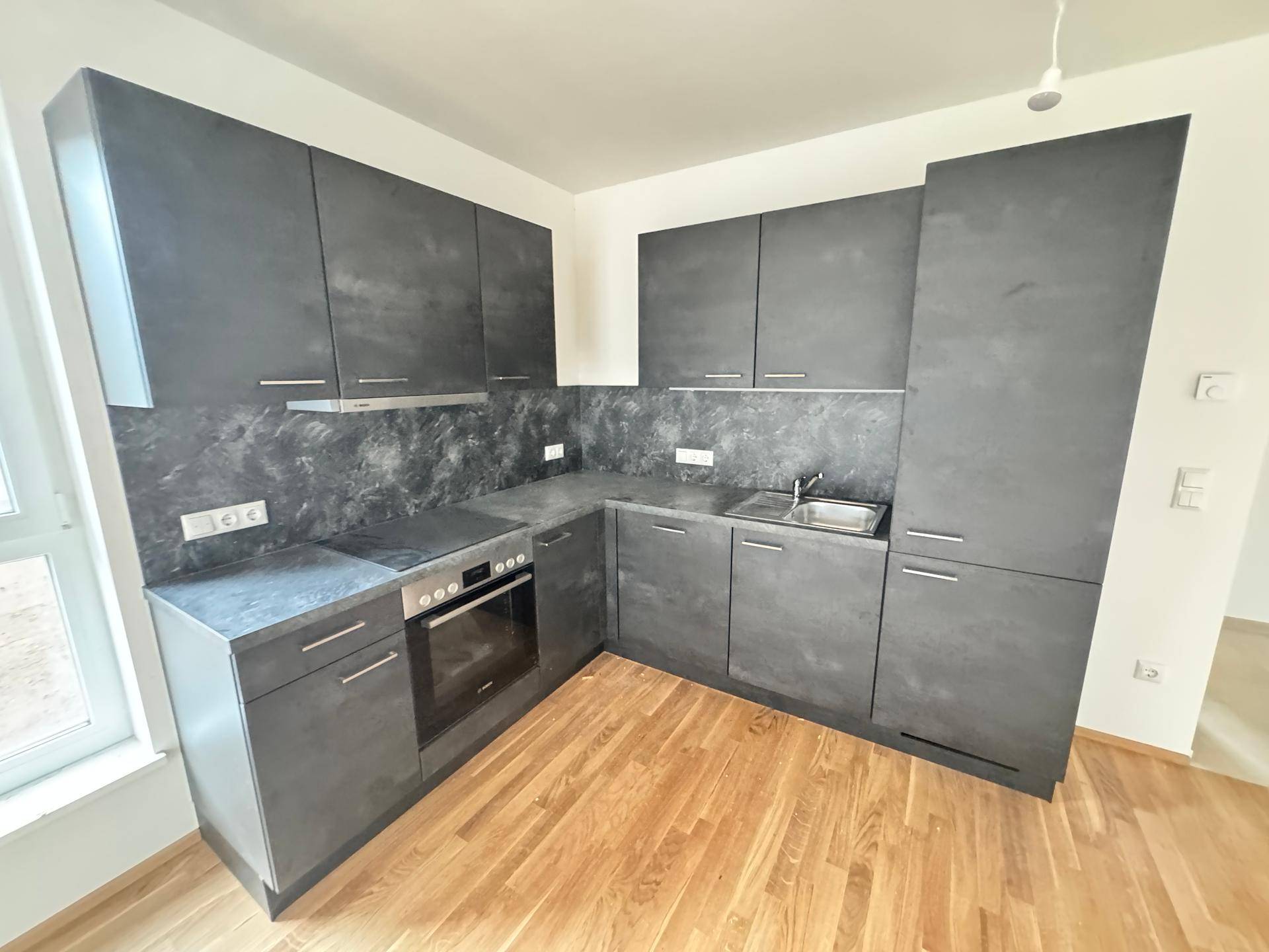 Moderne Einbauküche in Anthrazit mit Kochfeld, Backofen und Spüle, bereit zur Nutzung.