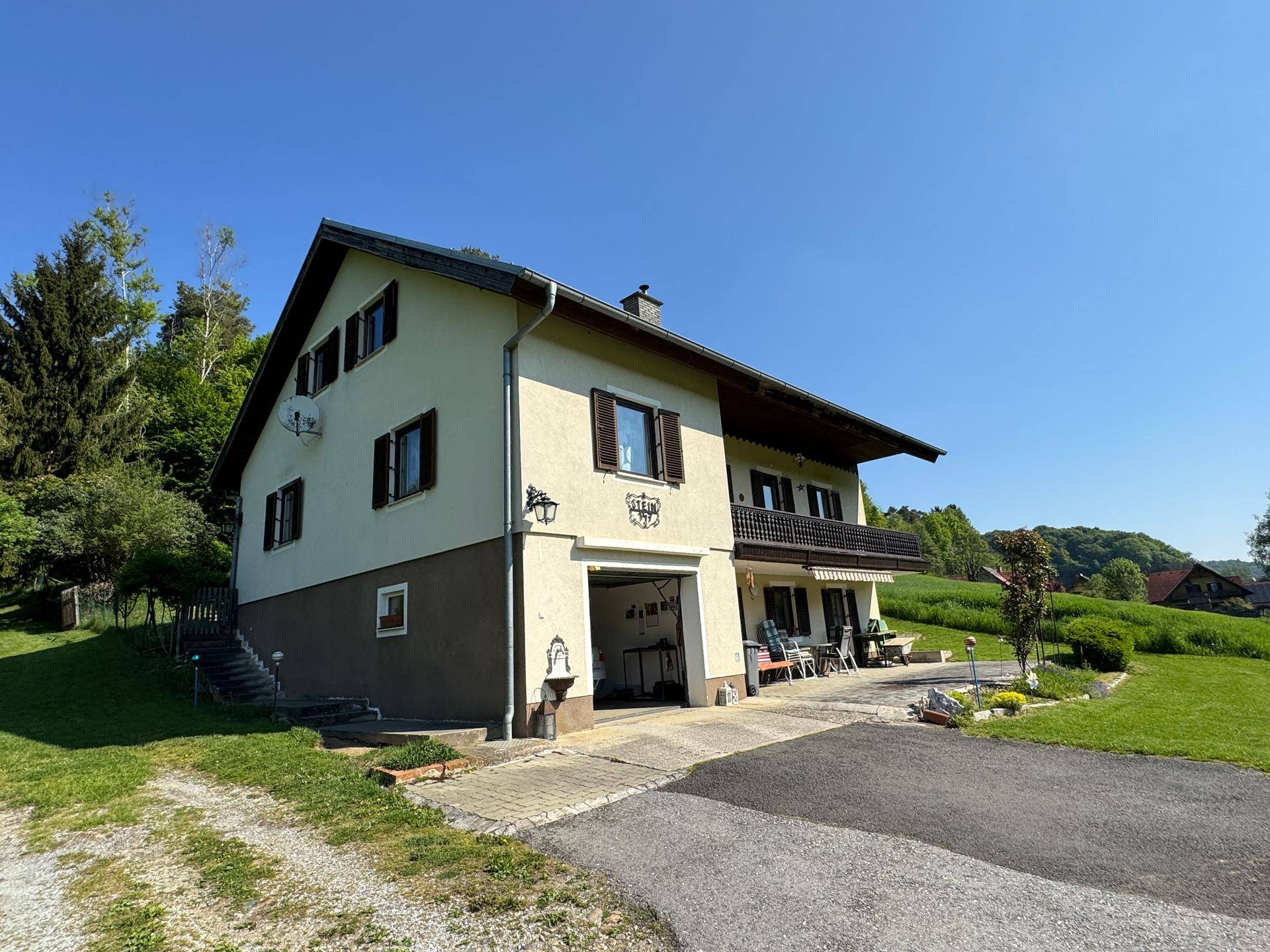 Ansicht des Hauses von der Seite mit Garage, Balkon und einer möblierten Terrasse im Grünen.