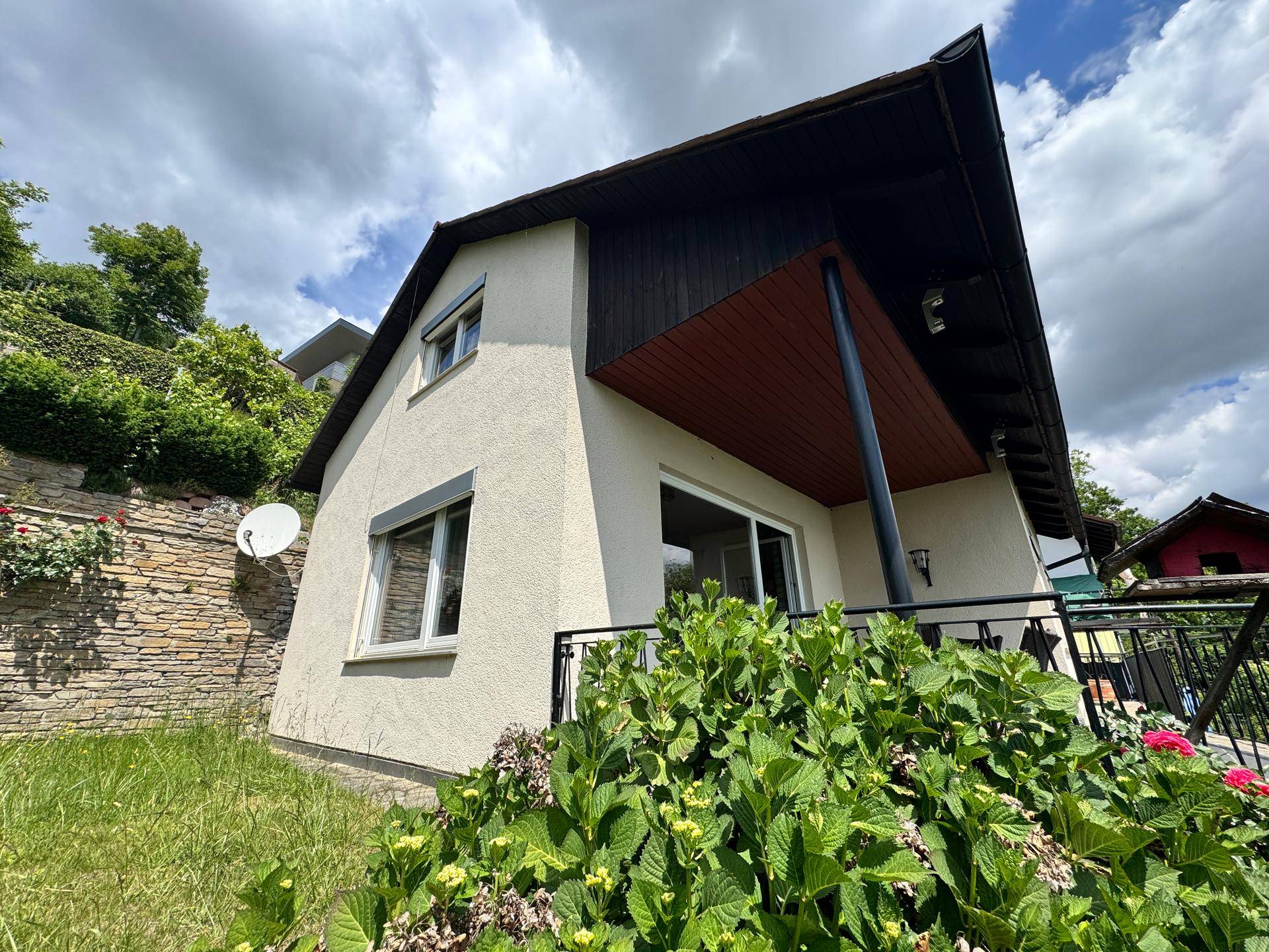 Hausfassade mit Balkon und Blick auf die grüne Umgebung unter bewölktem Himmel.