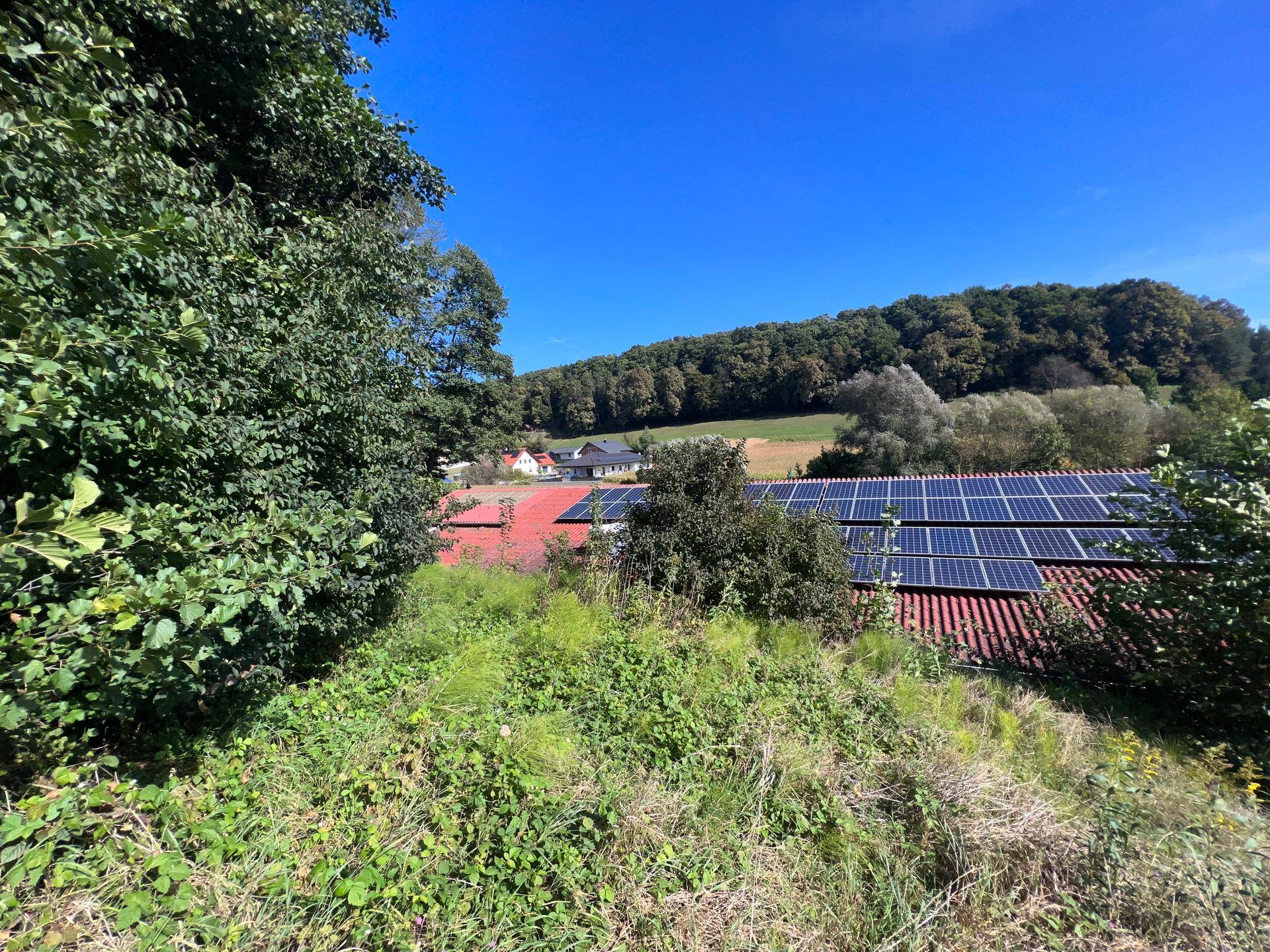 Weitläufige Ansicht des Daches mit Solaranlagen und der umliegenden grünen Landschaft und Feldern.