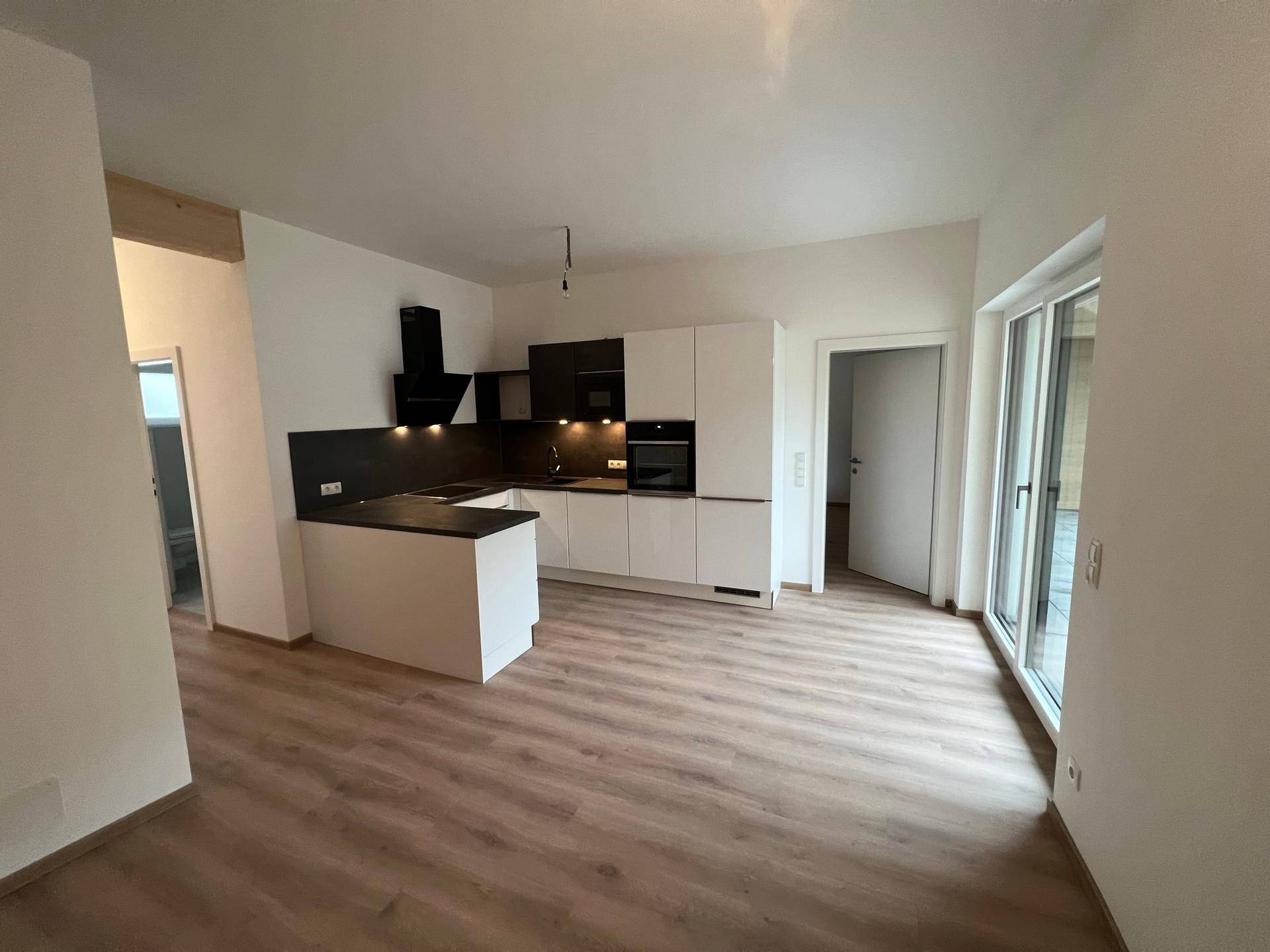 Geräumiger Wohnbereich mit offener Küche, Laminatboden und Zugang zu einem Außenbereich.