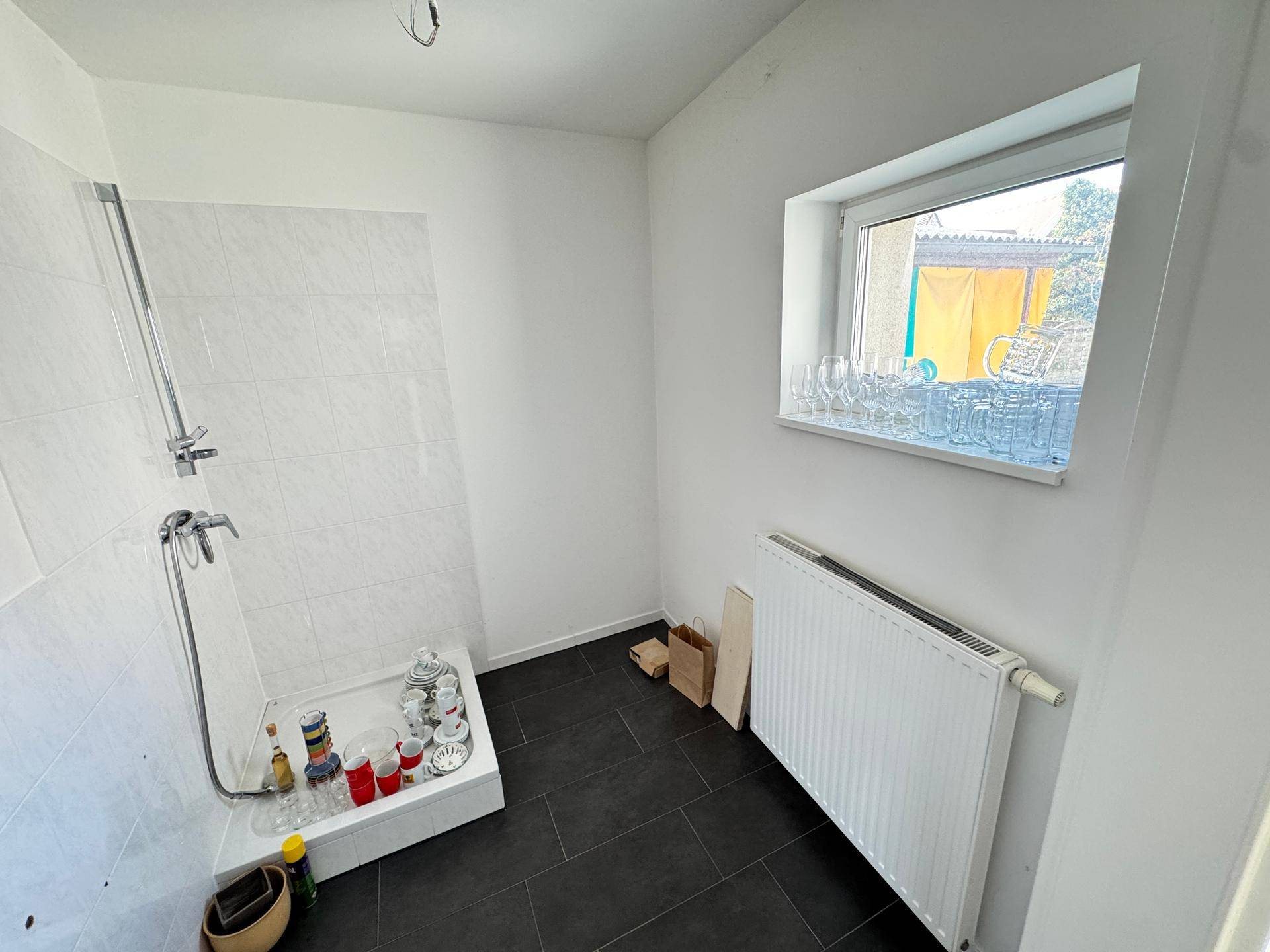 Einfacher Duschbereich mit Fenster, Heizkörper und Stauraum für diverse Gegenstände.