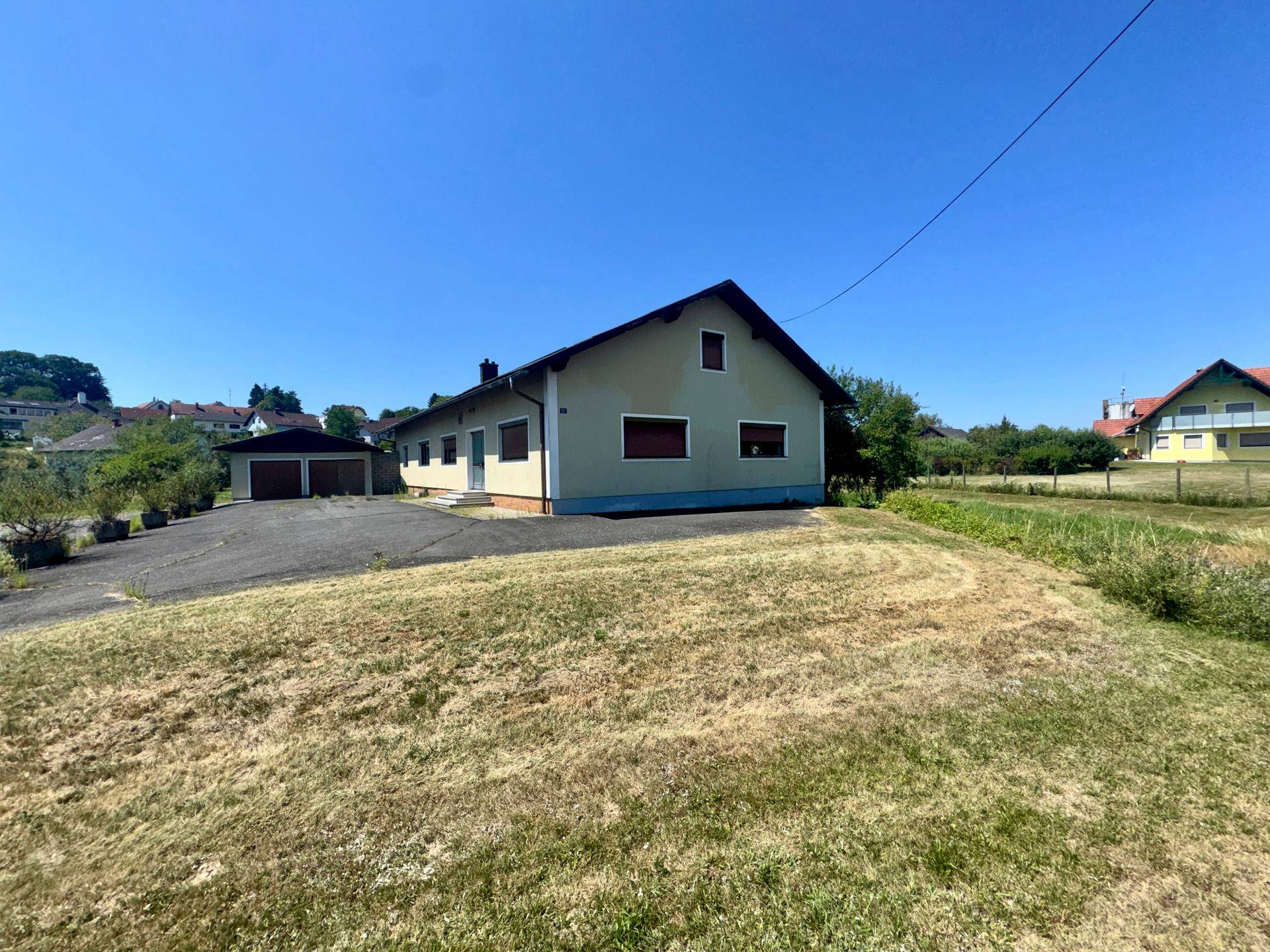 Einfamilienhaus mit großer Rasenfläche und angrenzender Garage an sonnigem Tag.