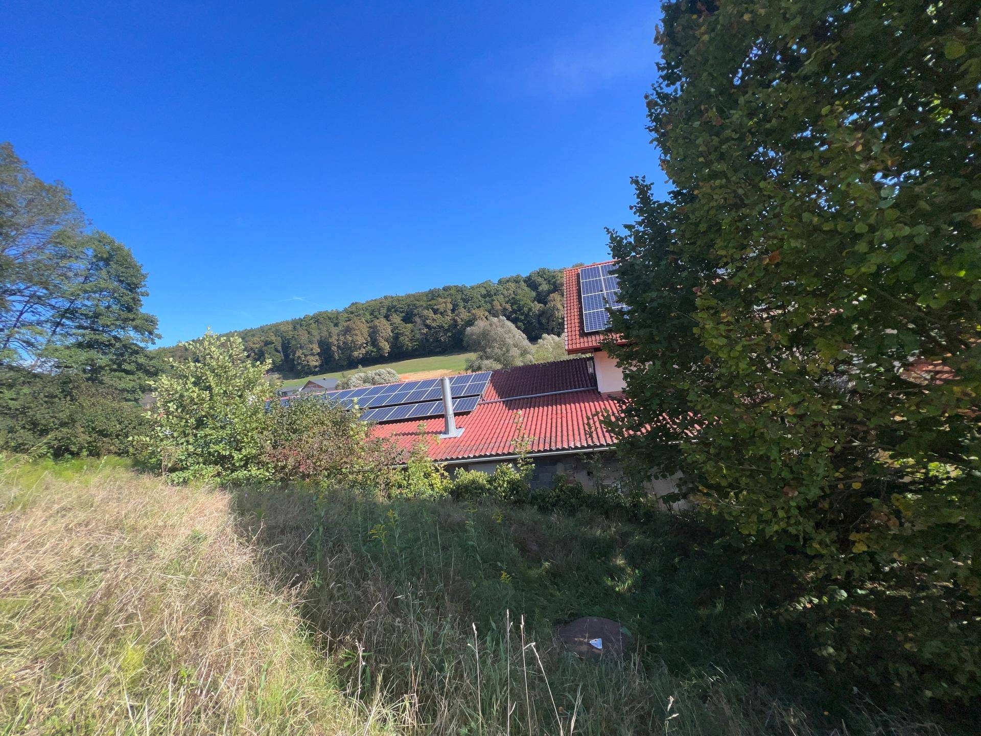 Dachansicht des Gebäudes mit zahlreichen Solarpaneelen und umgebender ländlicher Landschaft.