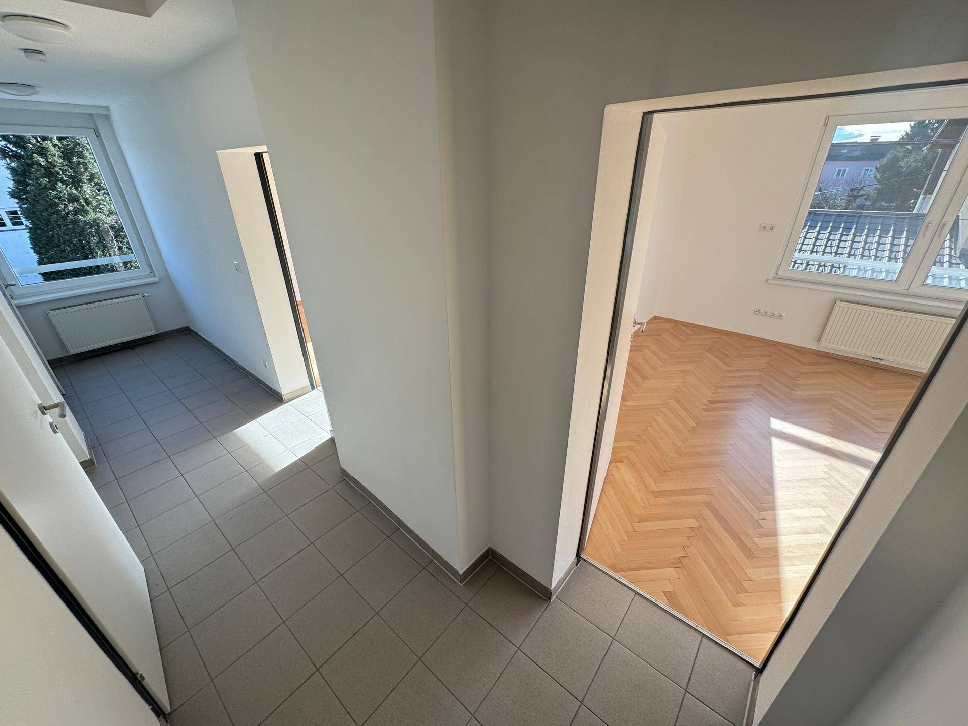 Heller Flur mit Fliesenboden und Blick in angrenzende Zimmer mit Parkett.