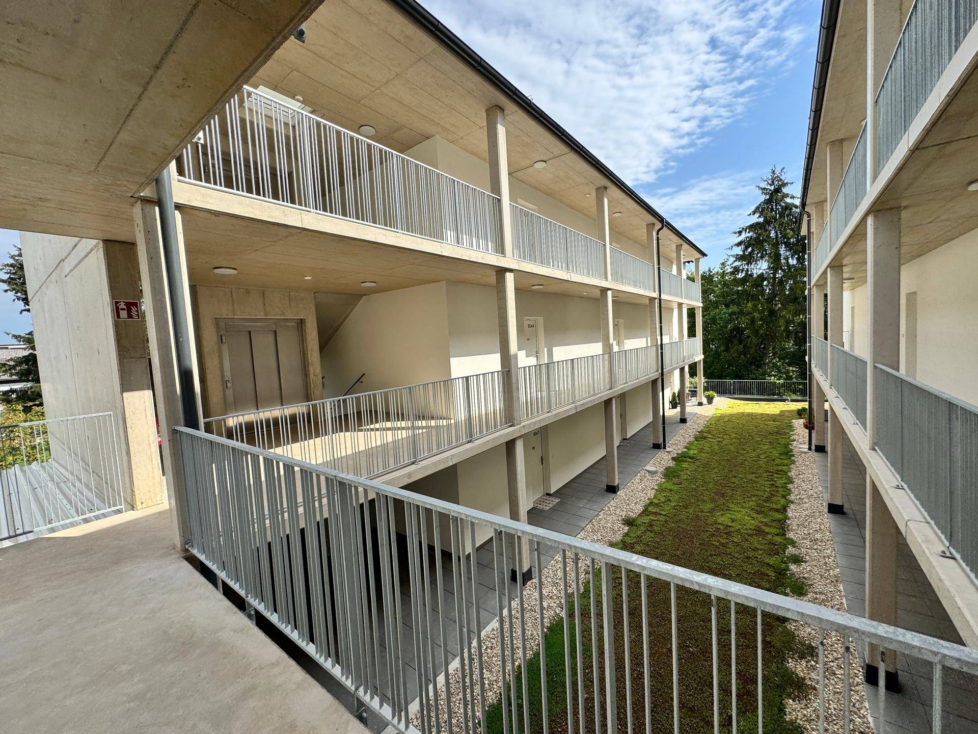 Offener Laubengang im Obergeschoss mit Blick auf den Aufzug und den begrünten Innenhof.