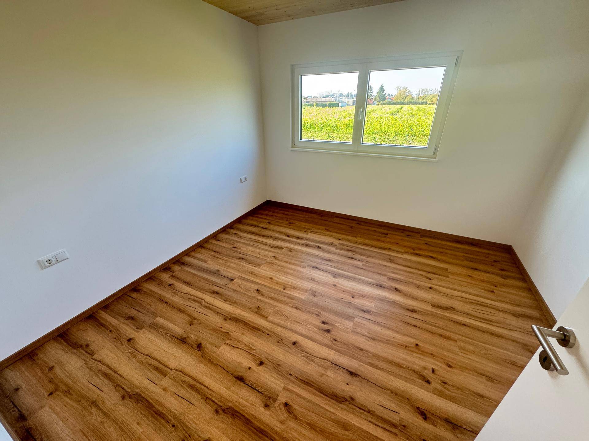 Helles Schlafzimmer mit Laminatboden und Fenster mit Blick ins Grüne.