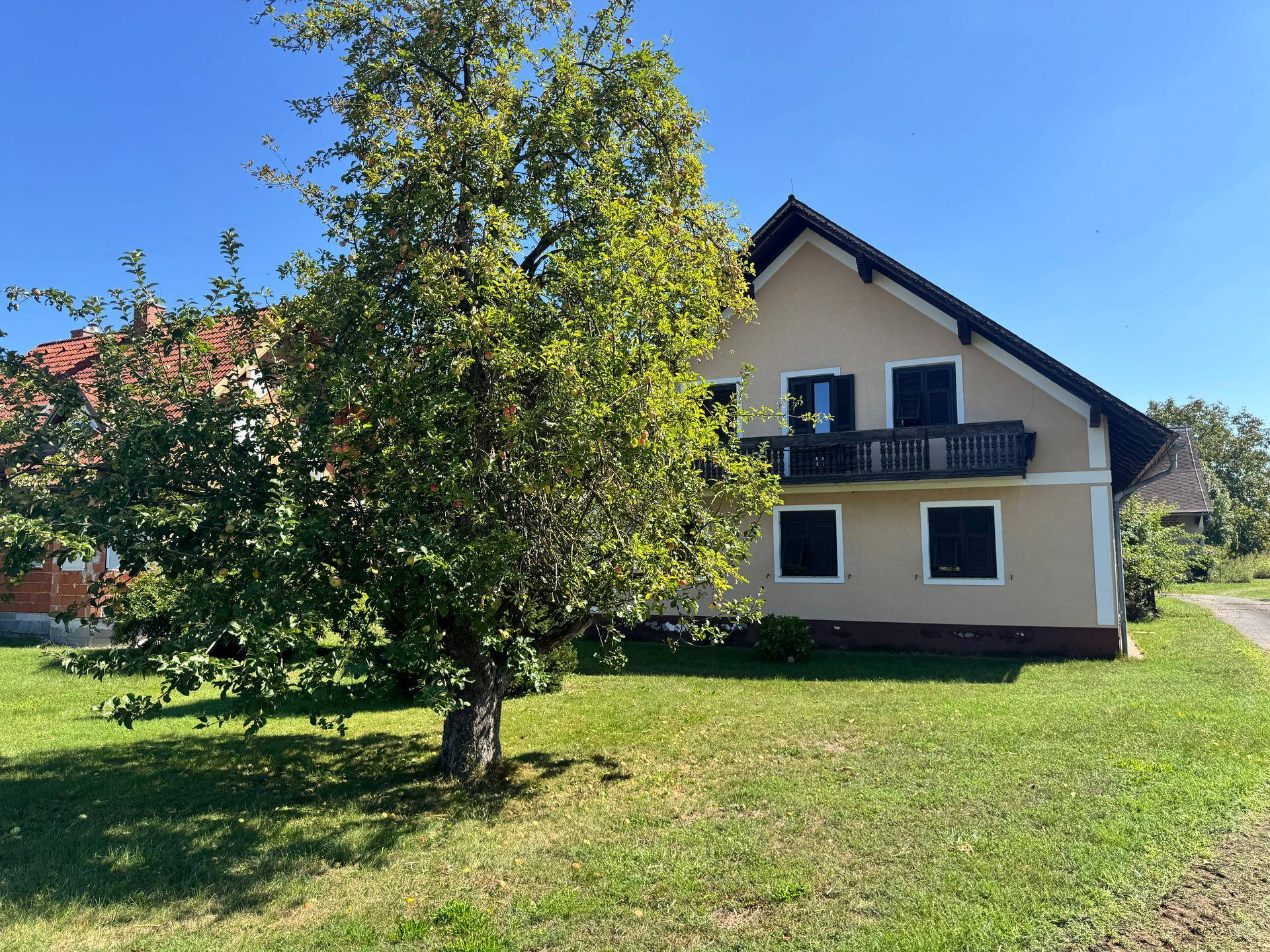 Traditionelles Landhaus mit Balkon und großem Baum auf grünem Grundstück.