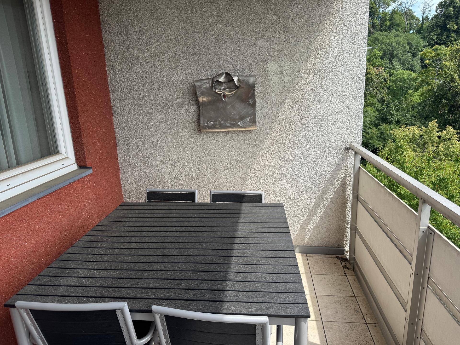 Möblierter Balkon mit Esstisch und Stühlen, bietet einen ruhigen Blick ins Grüne.
