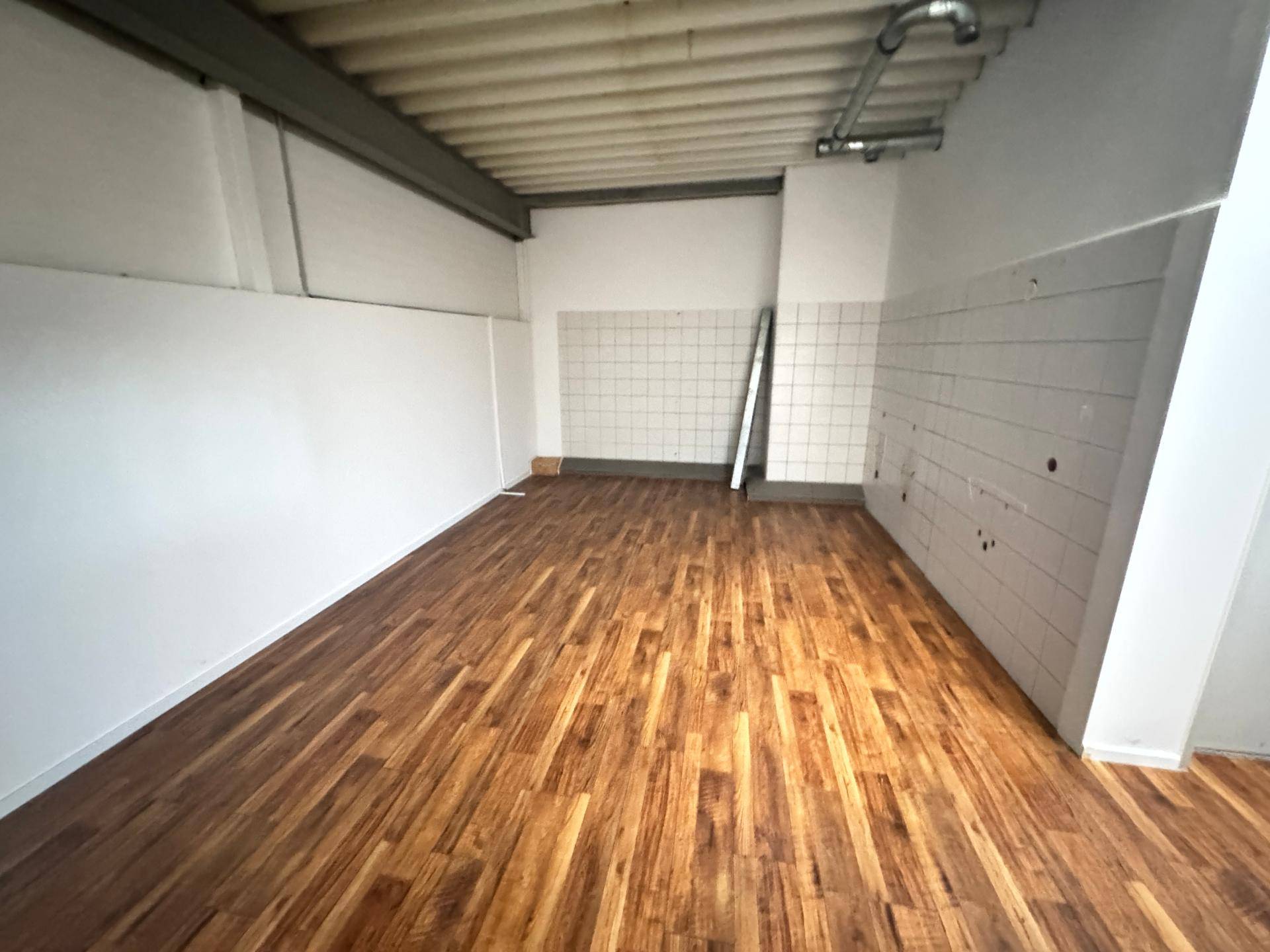 Einfacher Abstellraum mit Holzboden und teilweise gefliesten Wänden, ideal für Lagerzwecke.