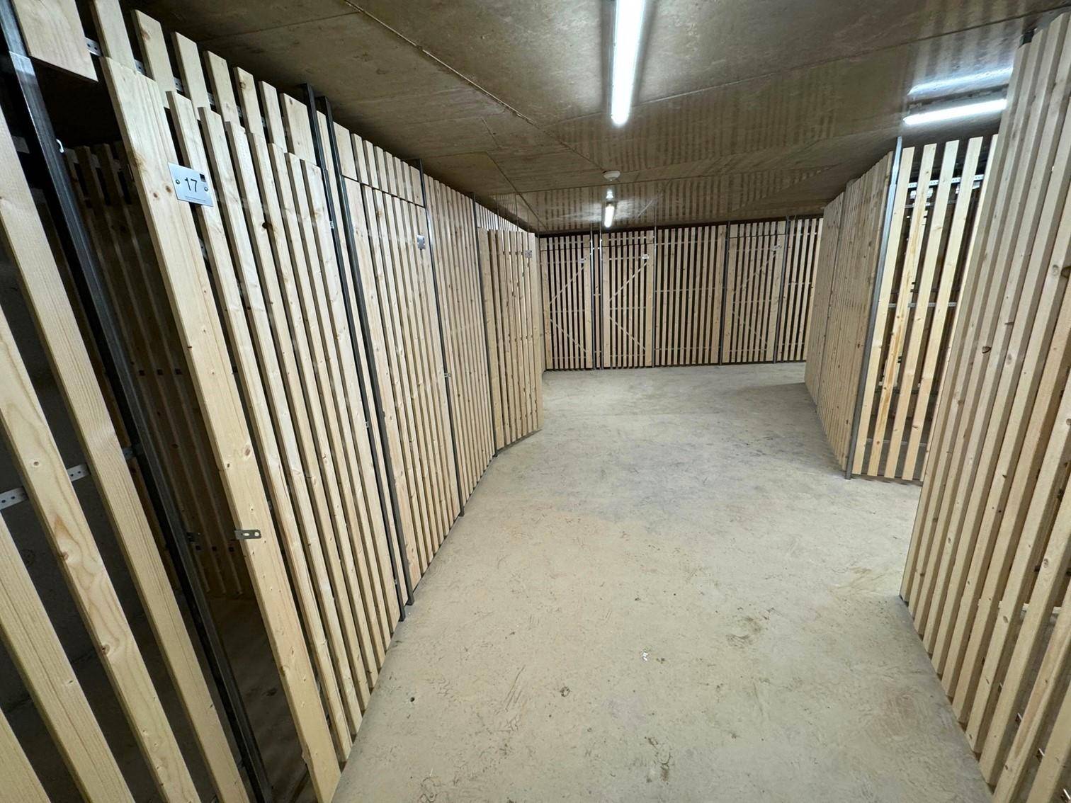 Kellerabteil mit Holzlattenwänden und Betonboden, ideal für zusätzlichen Stauraum.