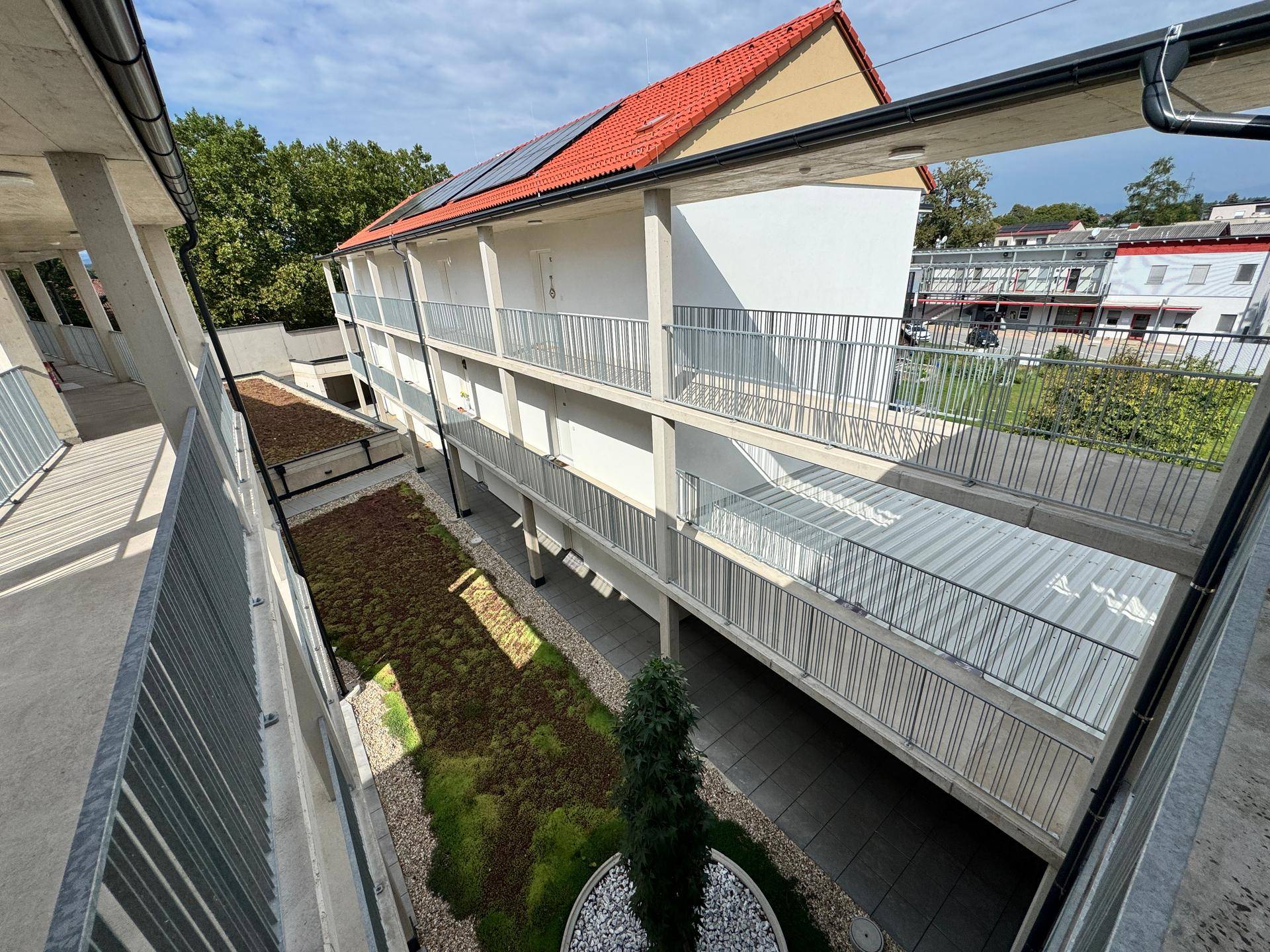 Blick von oben auf den begrünten Innenhof eines modernen Wohnkomplexes mit Balkonen.