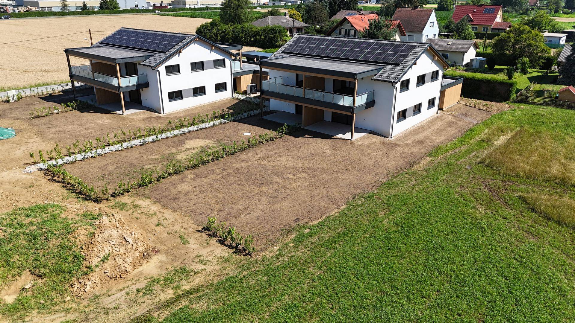 Luftaufnahme von zwei modernen Doppelhaushälften mit Solaranlagen und unbebauten Gärten.
