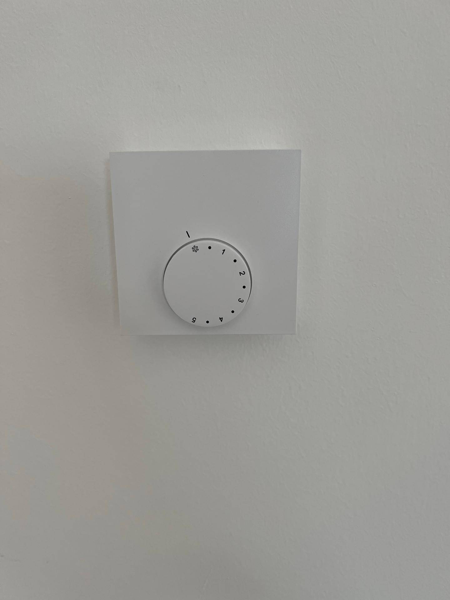 Nahaufnahme eines modernen Thermostats an einer weißen Wand, zur Steuerung der Raumtemperatur.