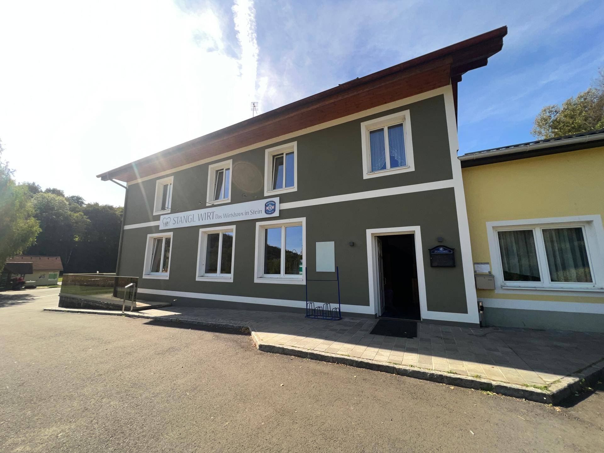 Vorderansicht des Gebäudes mit Sonneneinstrahlung und dem Schriftzug "Stangl Wirt".