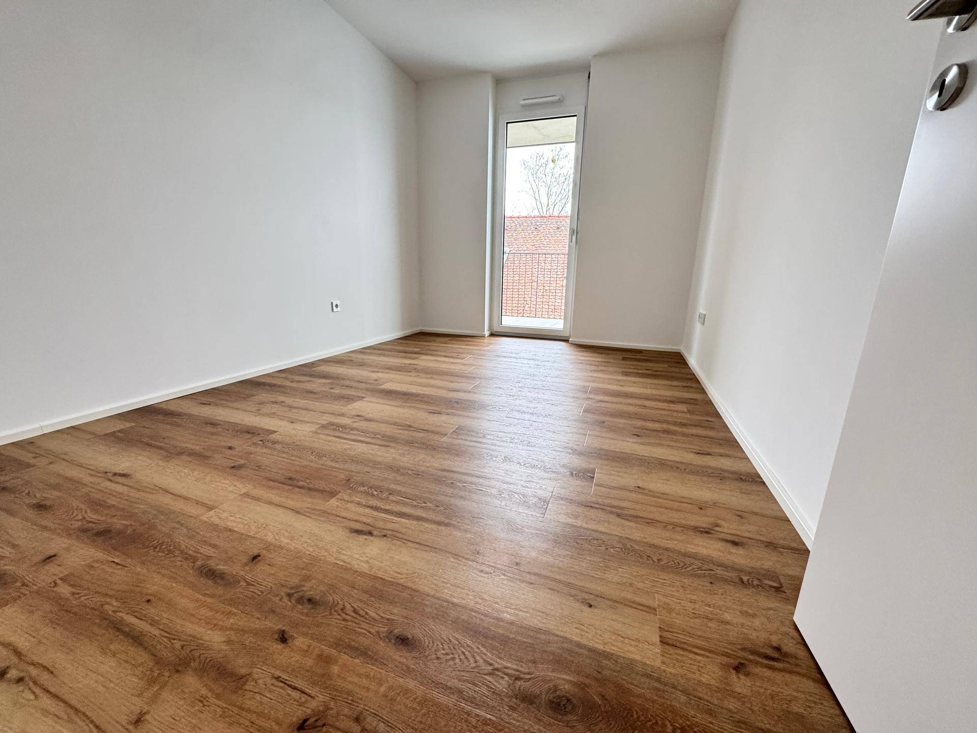 Leeres Schlafzimmer mit Holzboden und Fenster, das einen Blick ins Grüne ermöglicht.