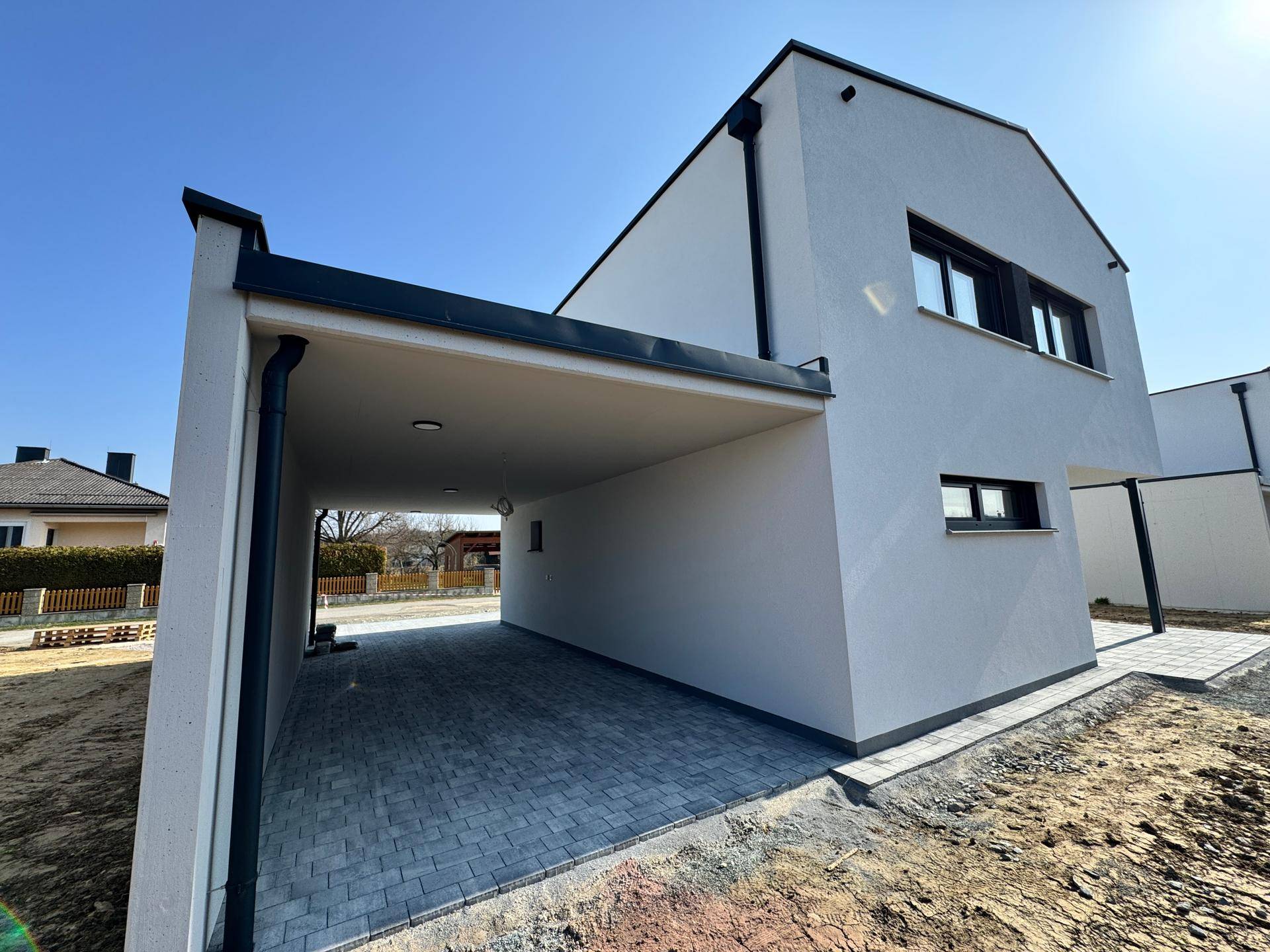 Integrierter Carport mit gepflastertem Boden und Zugang zum modernen Einfamilienhaus.