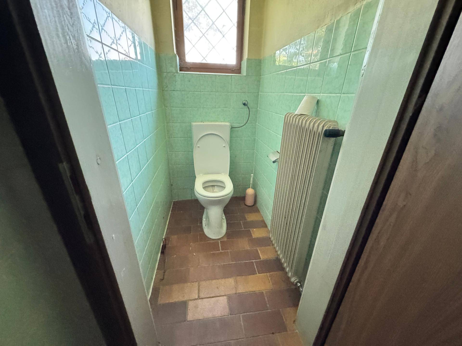Kleines WC mit grünen und braunen Fliesen, Toilette und Heizkörper.