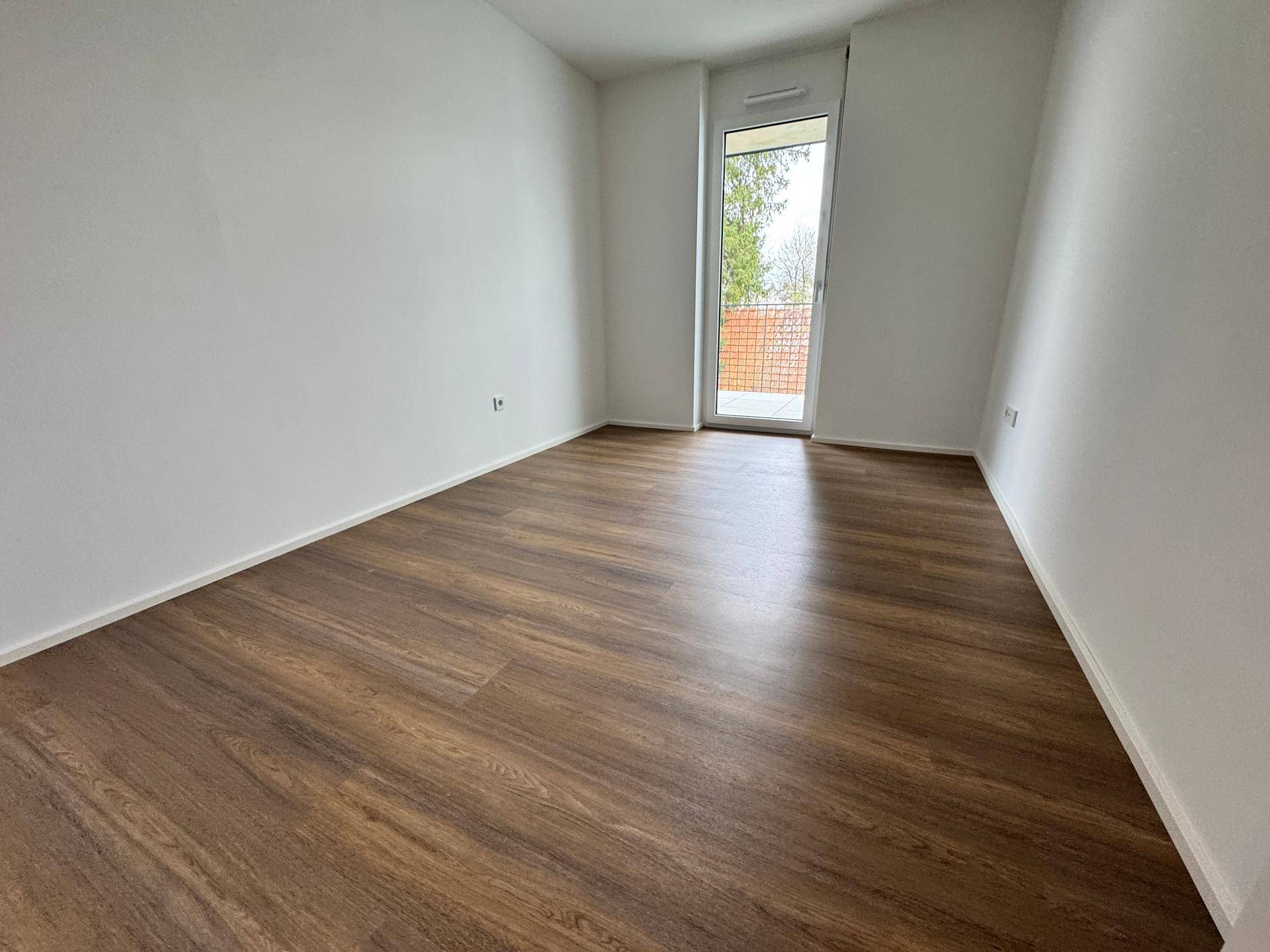 Geräumiges Schlafzimmer mit Laminatboden und Zugang zu einem kleinen Balkon.