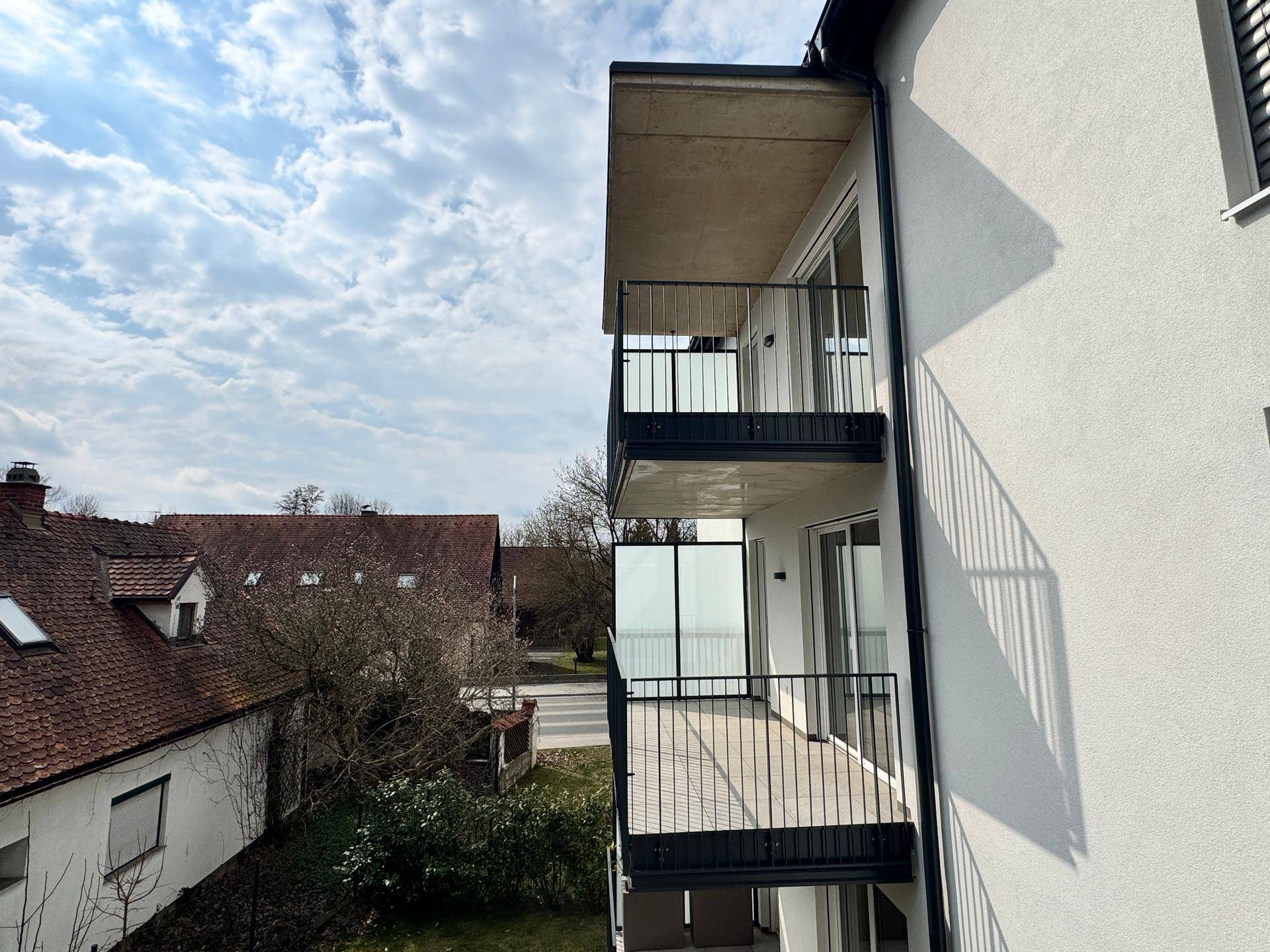 Seitenansicht eines Neubaus mit mehreren Balkonen und Blick auf die umliegende Nachbarschaft.