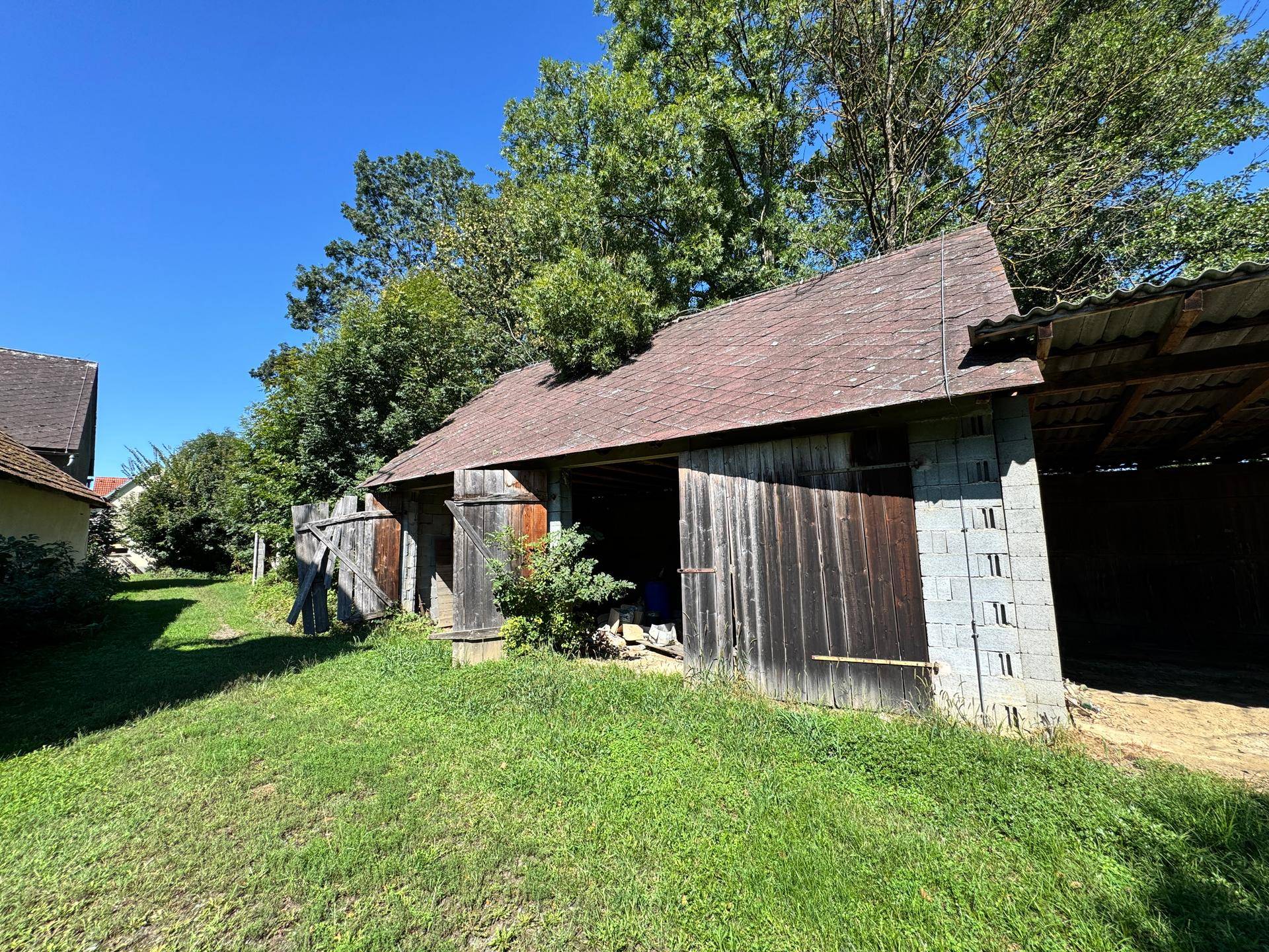 Altes Bauernhaus mit Holztüren und einem überdachten Bereich, umgeben von Grünflächen.
