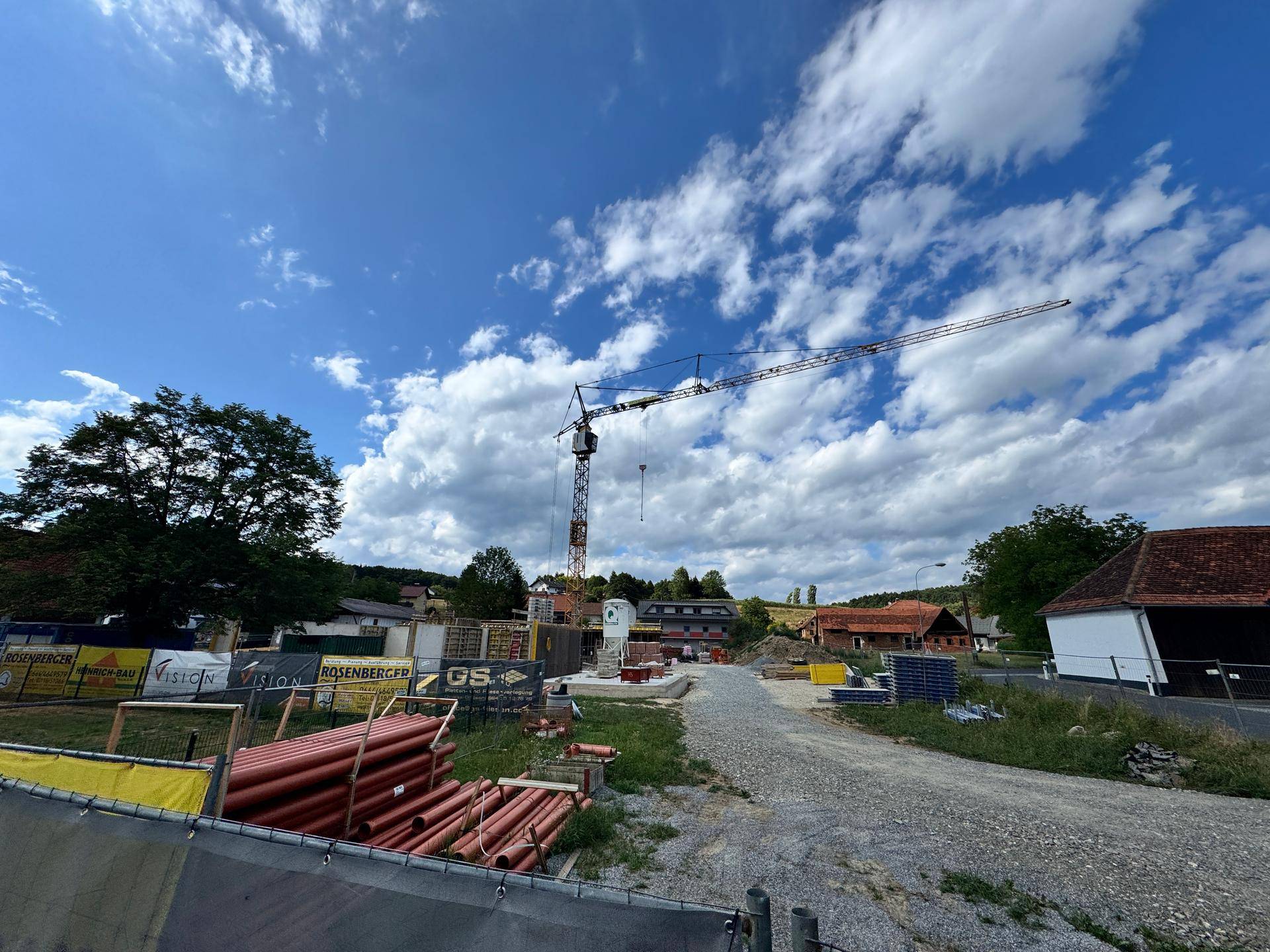 Übersicht der Baustelle mit einem großen Kran und gelagerten Rohren im Vordergrund.